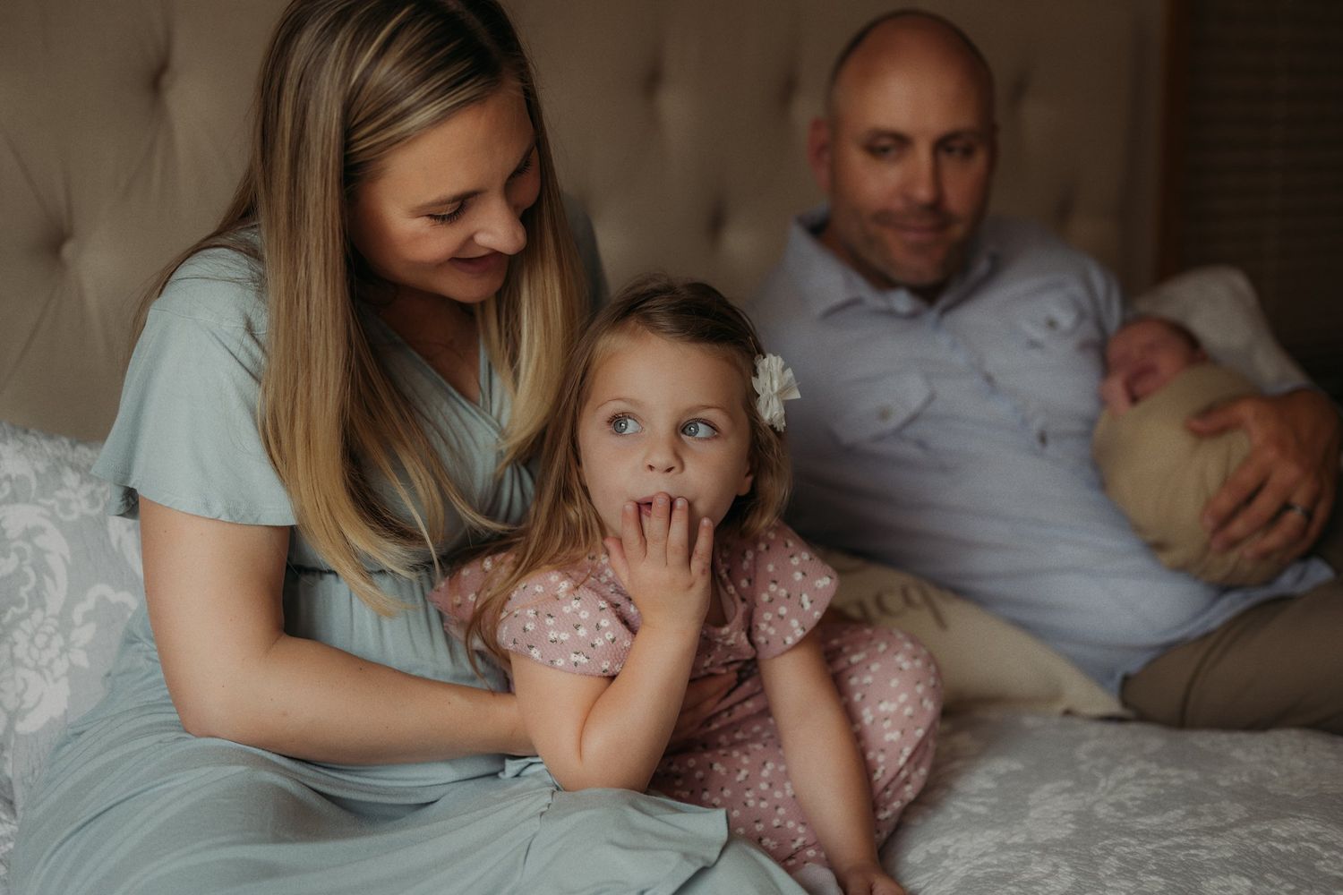 Candid family moment captured on bed with soft natural lighting.