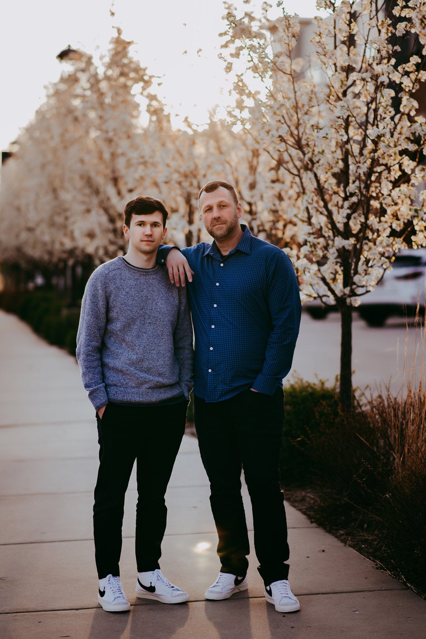 Two people stand together on sidewalk wearing coordinated casual outfits during sunset.