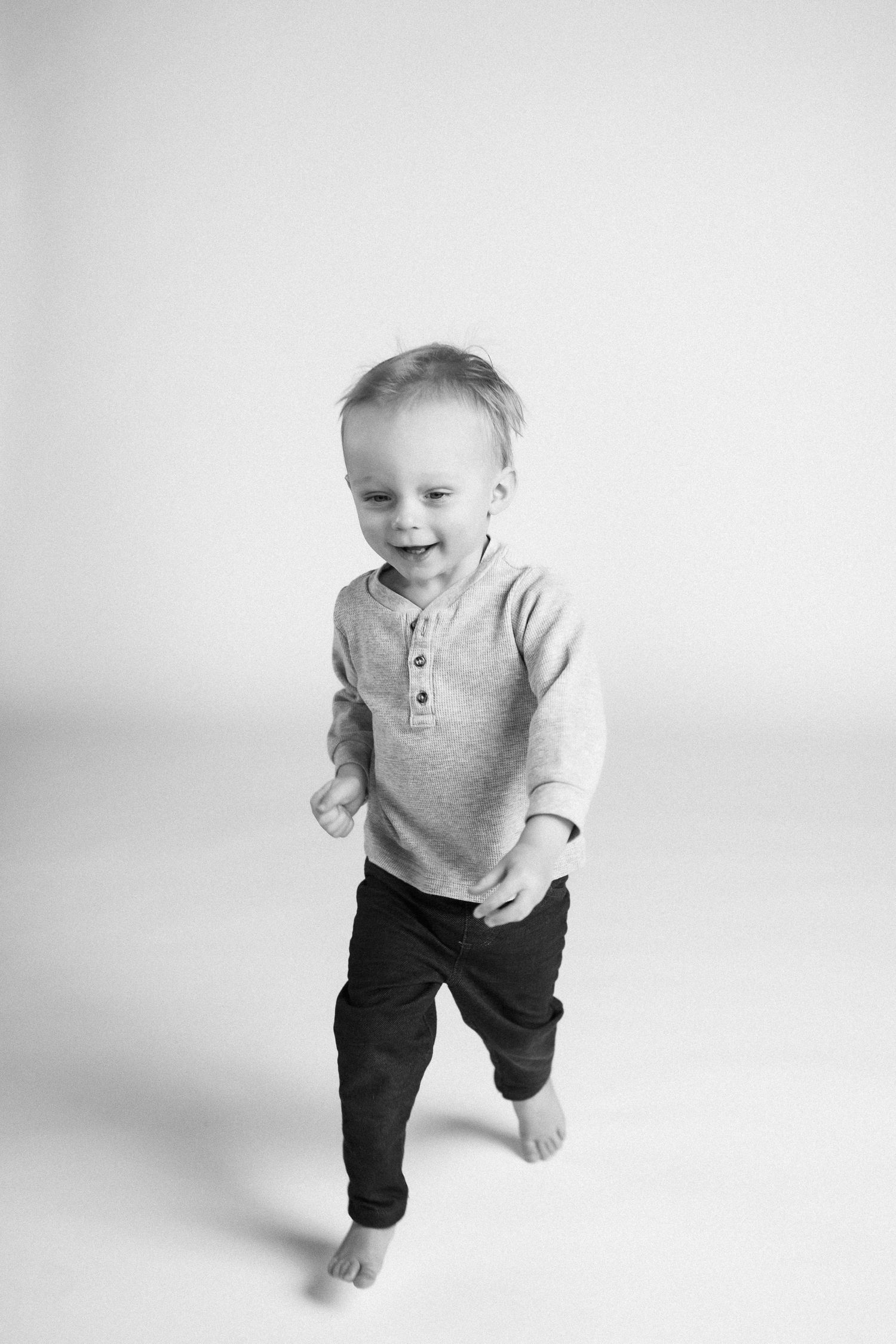 Black and white photo series showing a toddler in gray top and dark pants walking across white background.