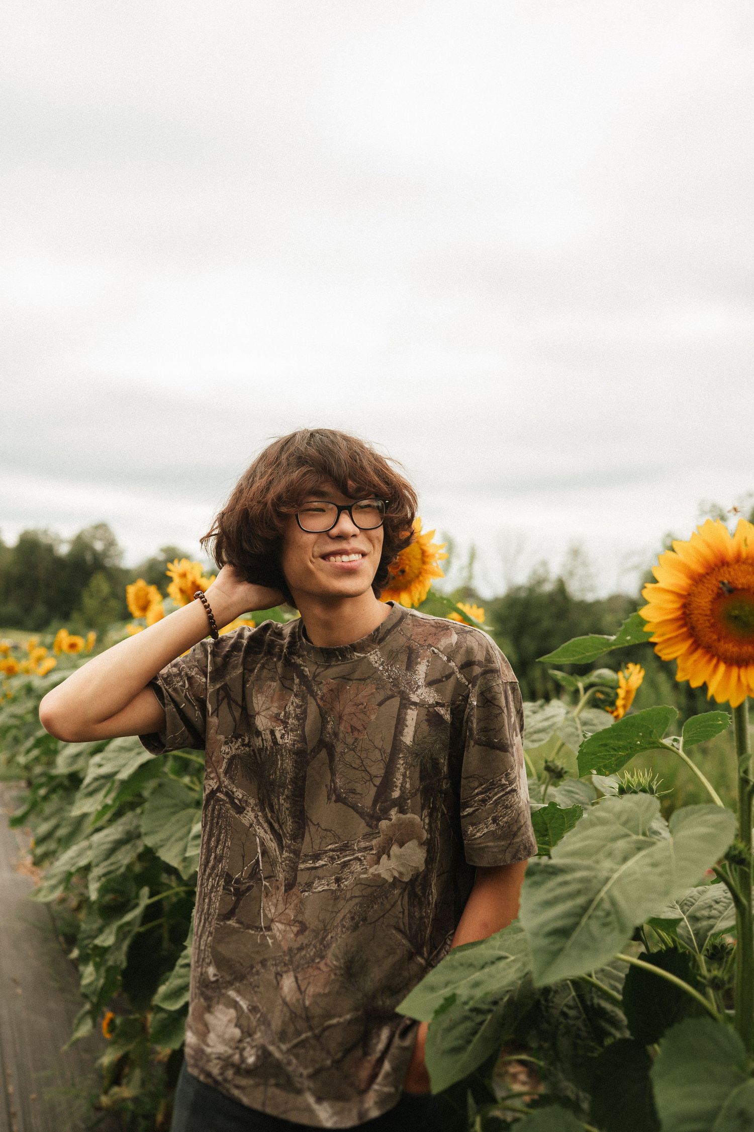 A series of portraits of someone wearing glasses and camouflage shirt in a blooming sunflower field.