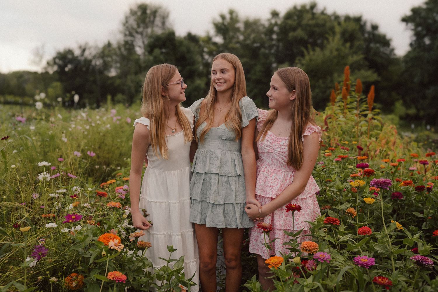 Three people laughing together in a wildflower meadow filled with colorful summer blooms and natural grasses.