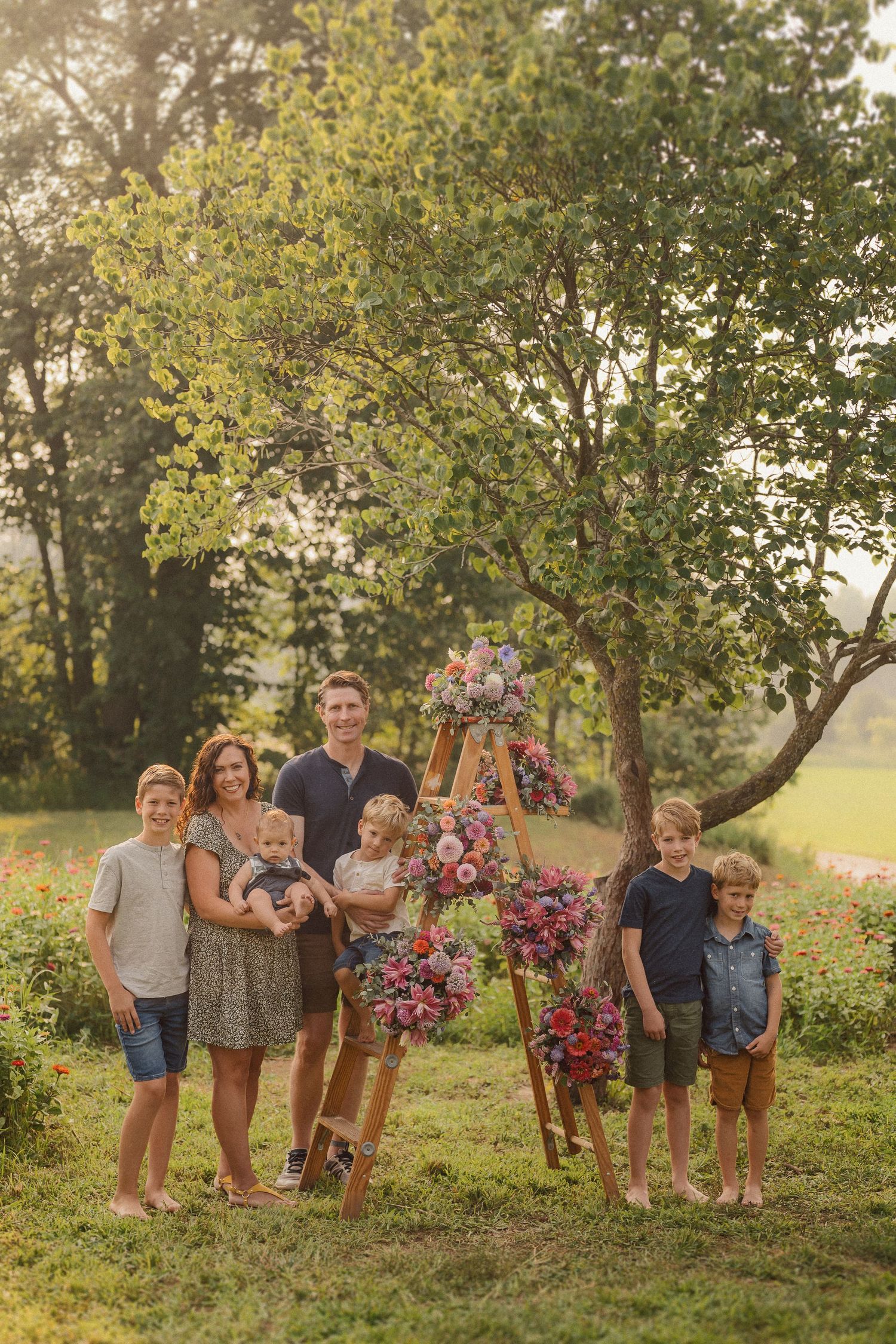Extended family gathering for portraits near a wooden arch adorned with pink flowers in an outdoor setting.