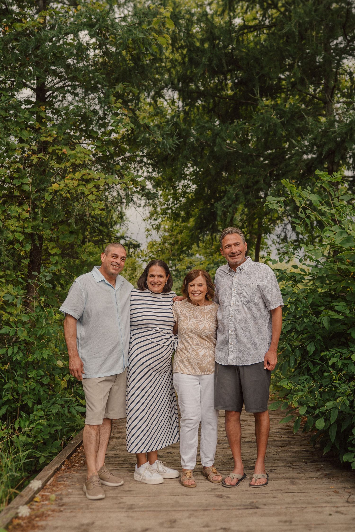 A group of people pose together on a wooden deck surrounded by lush green foliage and trees.