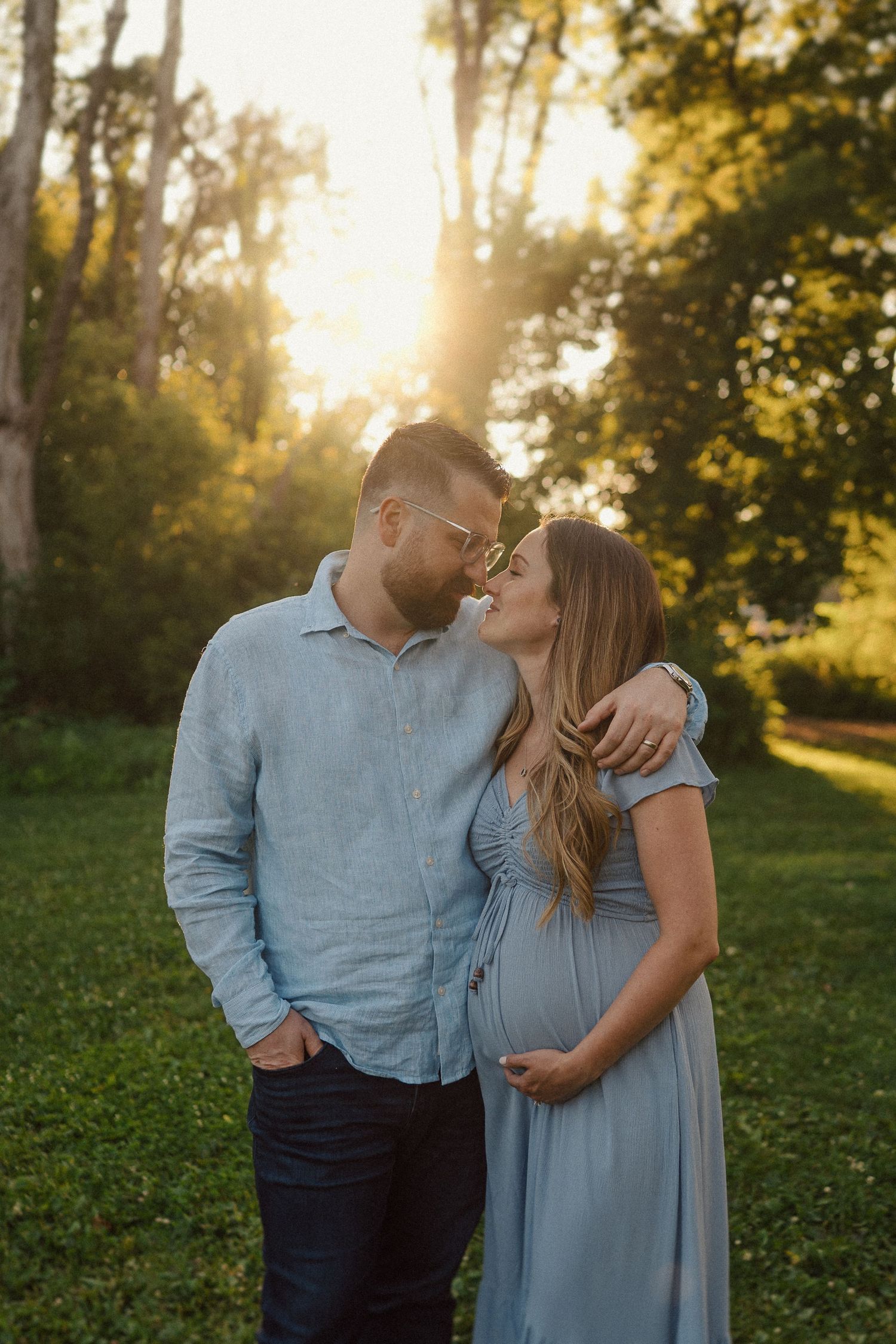 A couple wearing blue outfits shares an intimate moment during a golden hour portrait session in a grassy field.