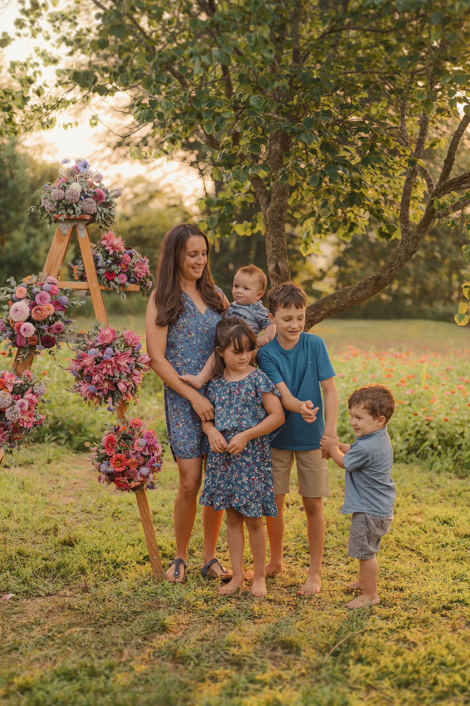 Children playing and laughing together near wooden ladder decorated with colorful flowers in garden setting.