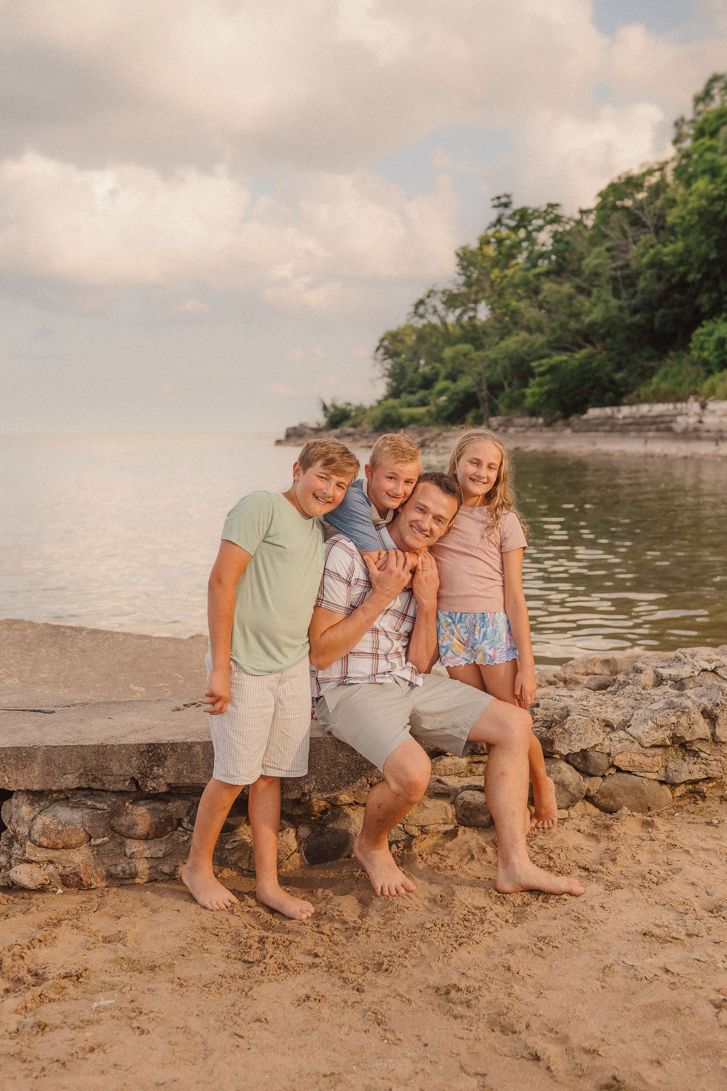 Four people share a casual moment while sitting together on a rocky beach during golden hour.