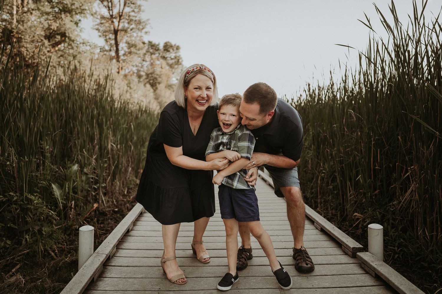 Family sharing a joyful moment together on wooden boardwalk surrounded by tall grass.