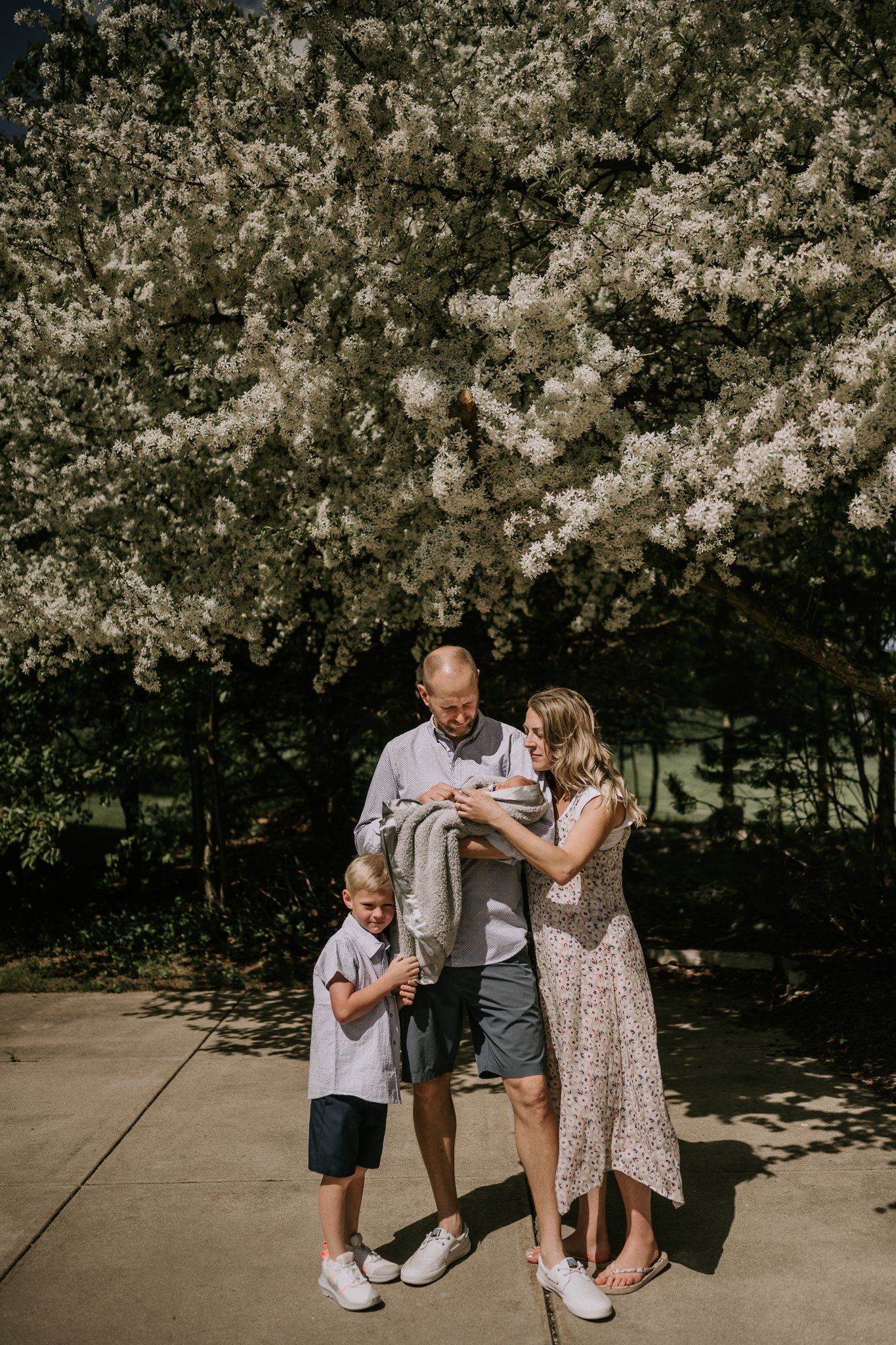 A family stands together under blooming cherry blossoms on a concrete path.