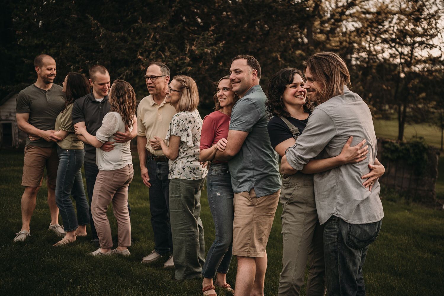 A group of people laugh together while standing in a line outdoors at dusk.