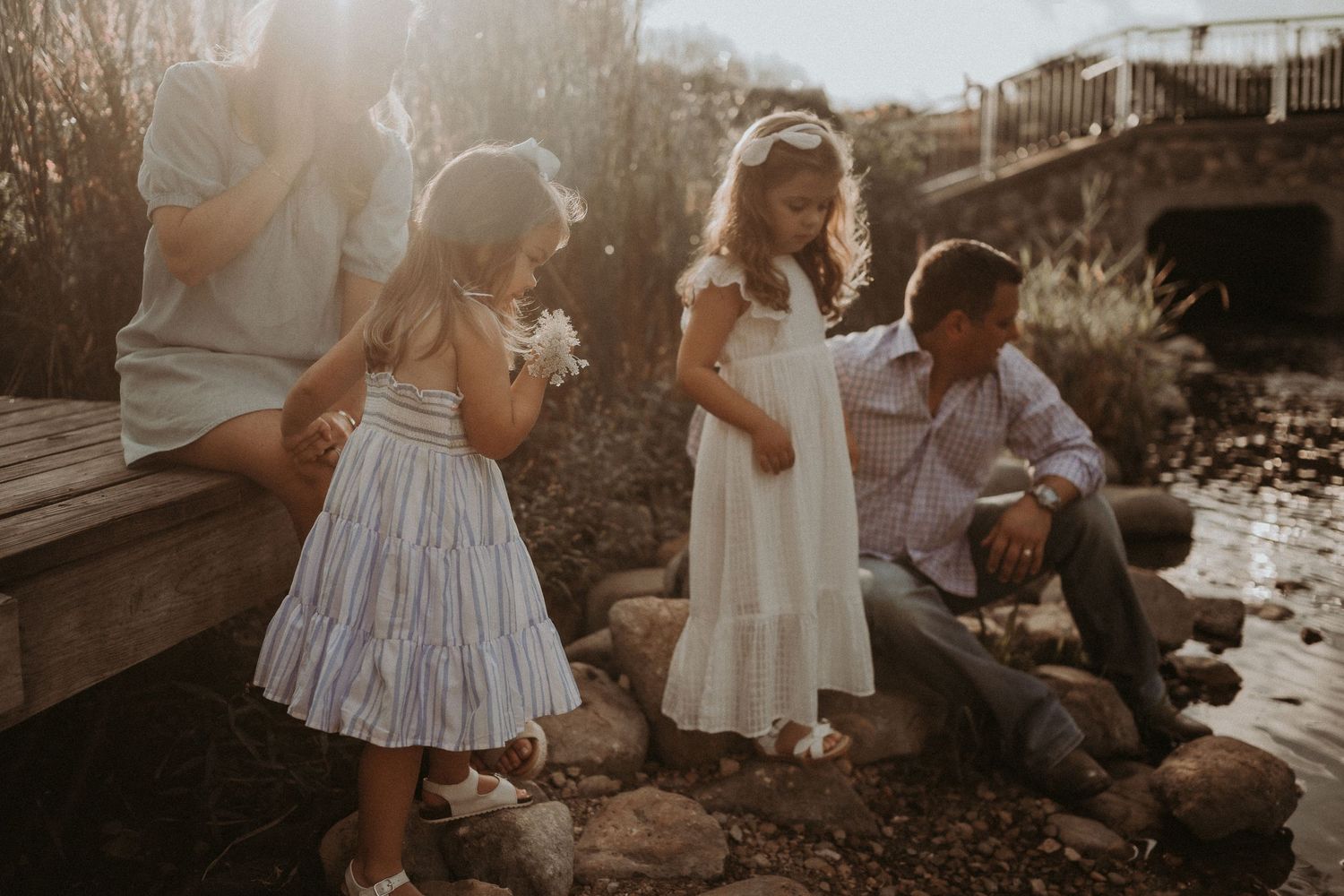 Family enjoying a casual moment together on rocks by the water during golden hour.
