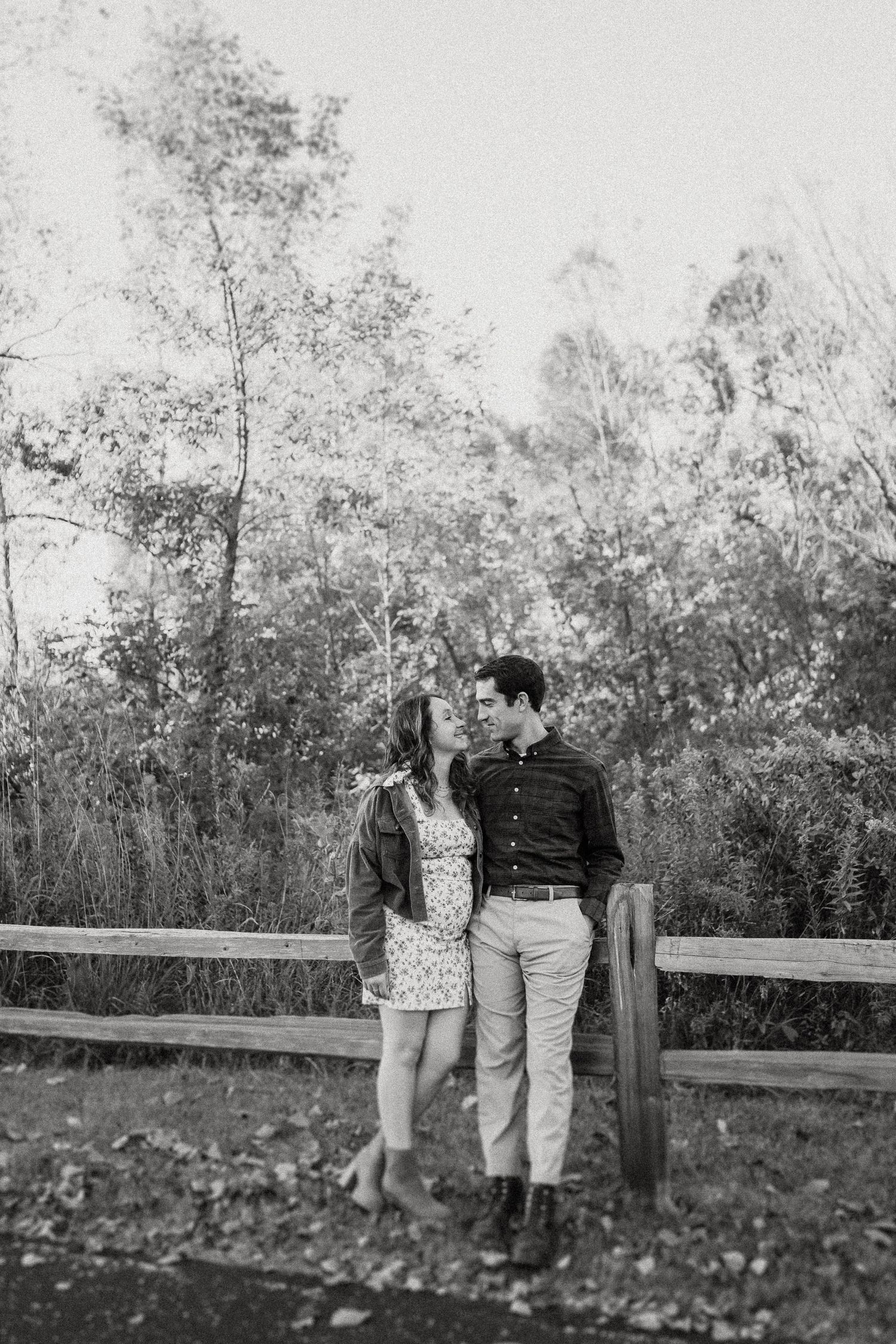 Black and white portrait of couple by rustic fence in natural setting.