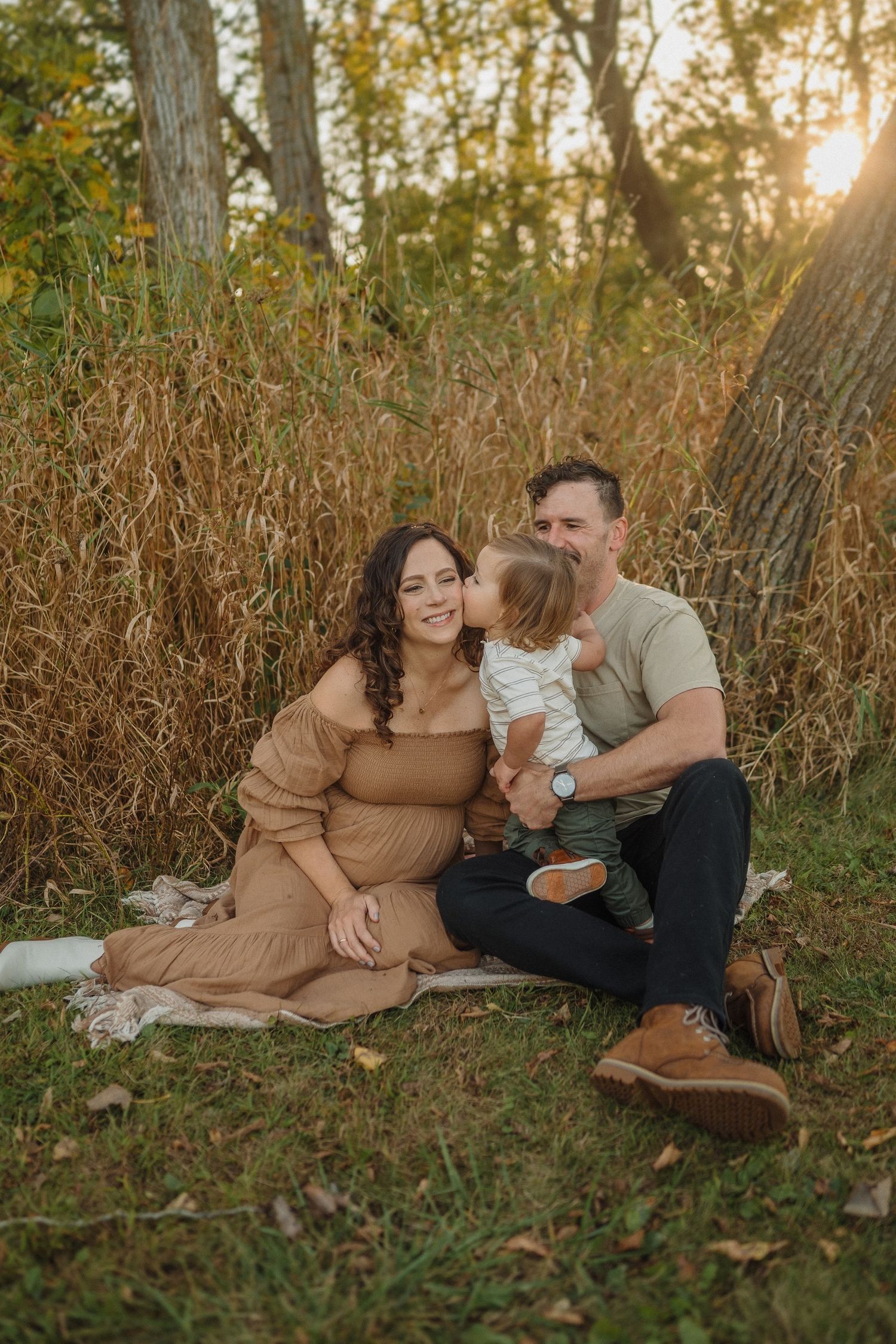 A family sitting together on a blanket amid tall grasses during a golden sunset.