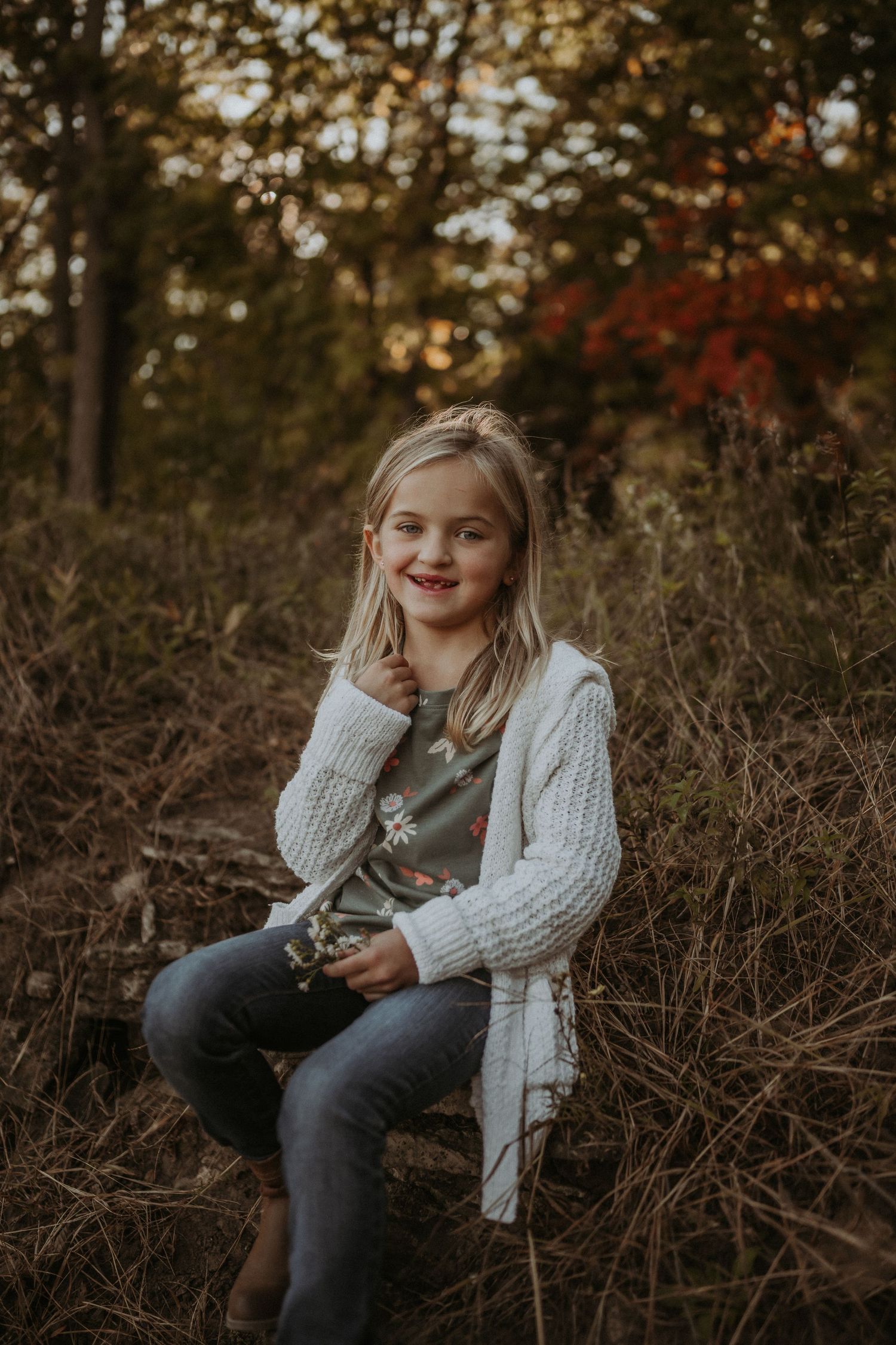 Candid outdoor portrait with cream cardigan against autumn trees and dried grass.