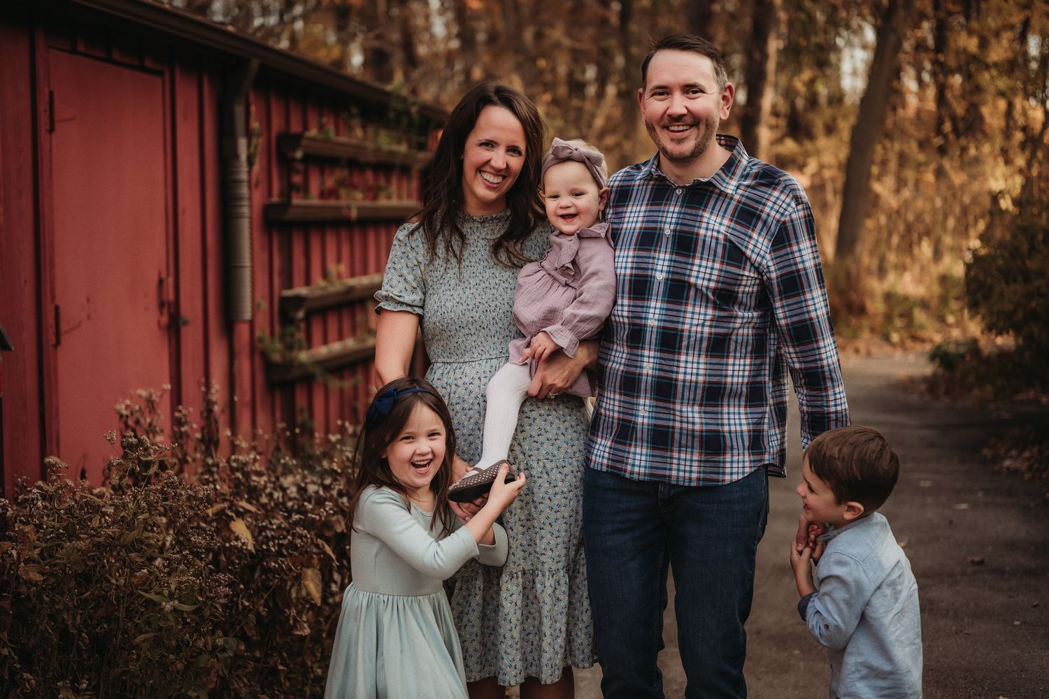 A family shares a candid moment together on a wooded path near a red building.