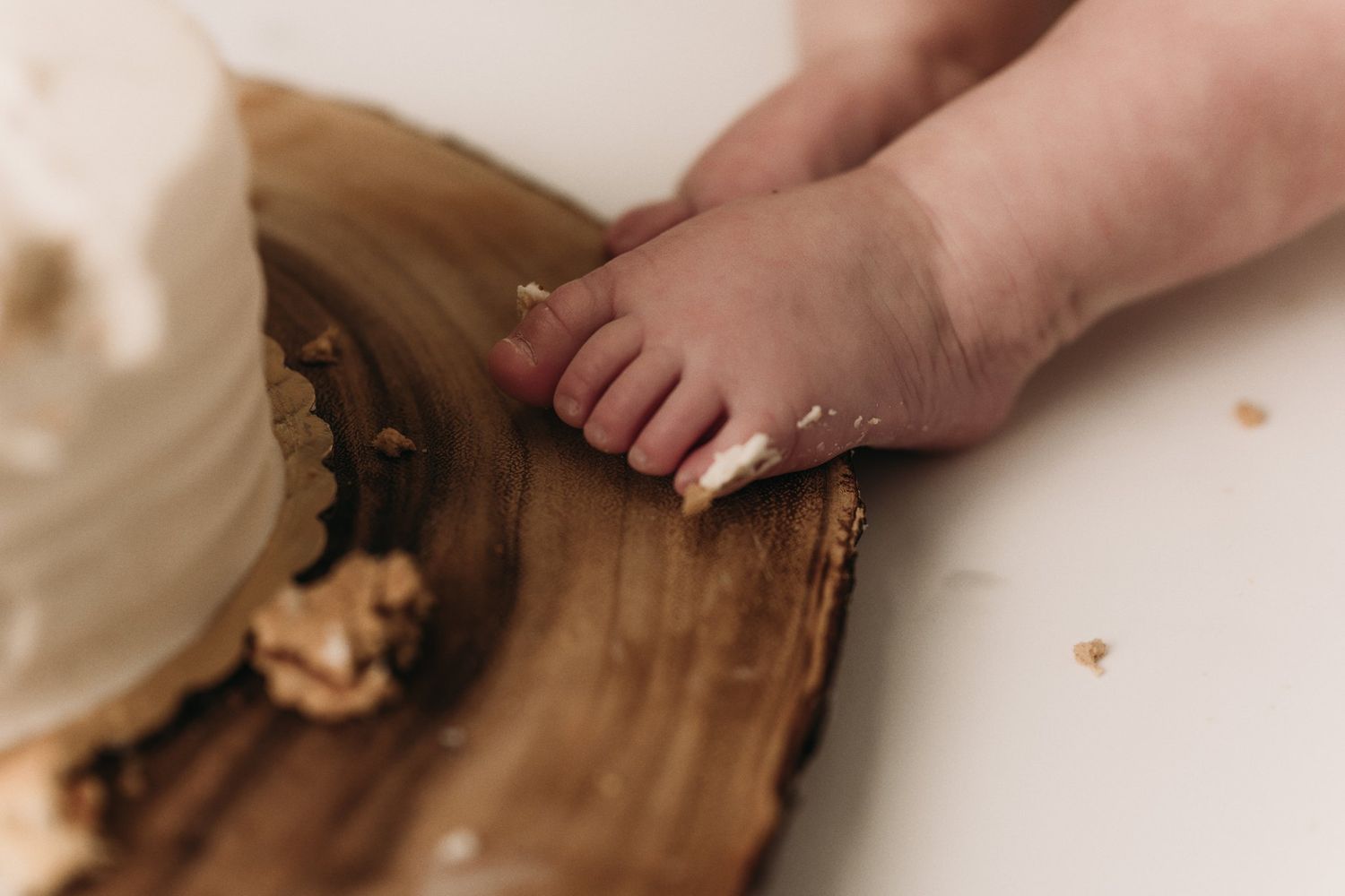 Close-up of tiny toes touching wooden slice with white cake.