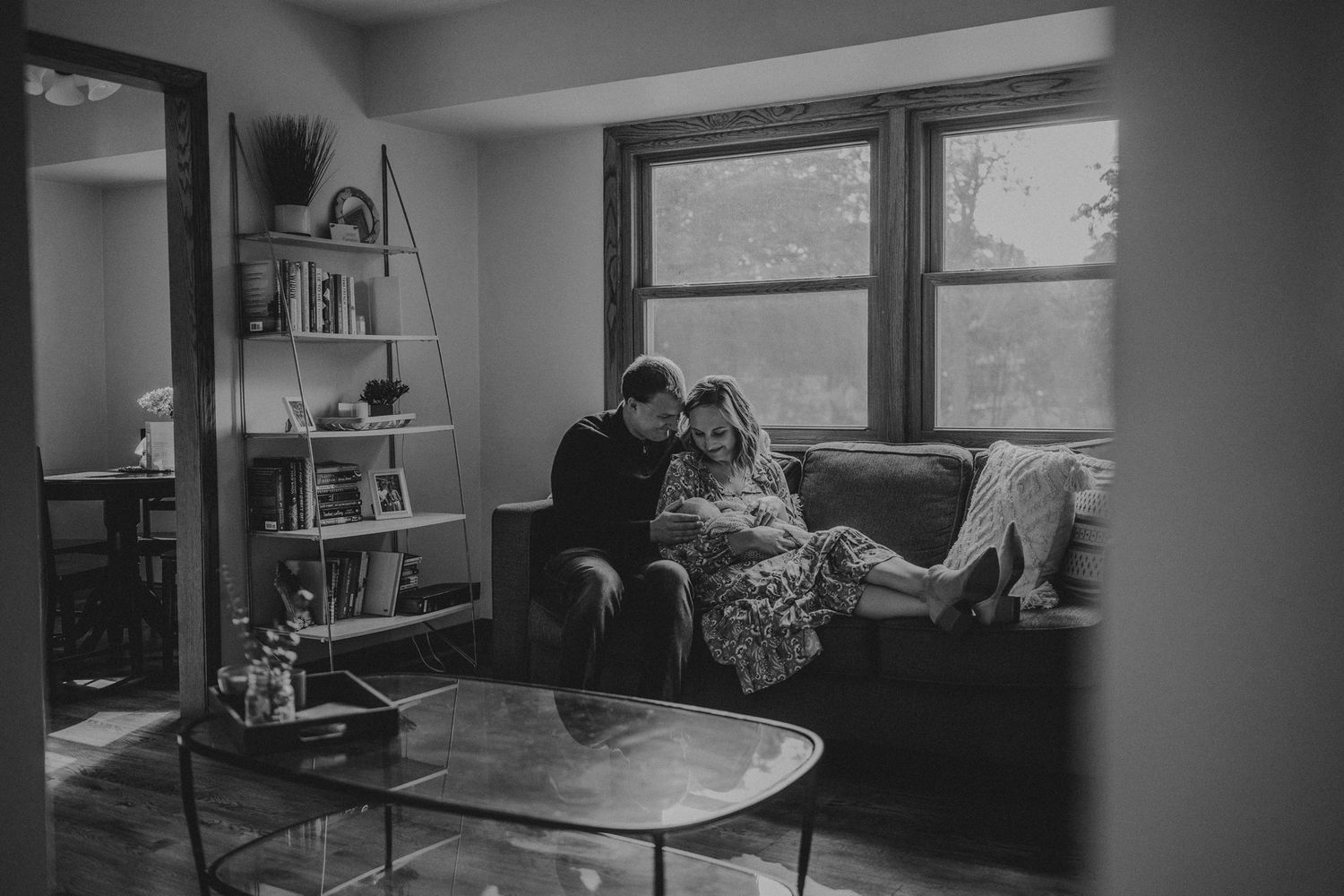 Black and white photo of family relaxing together on sofa by window.