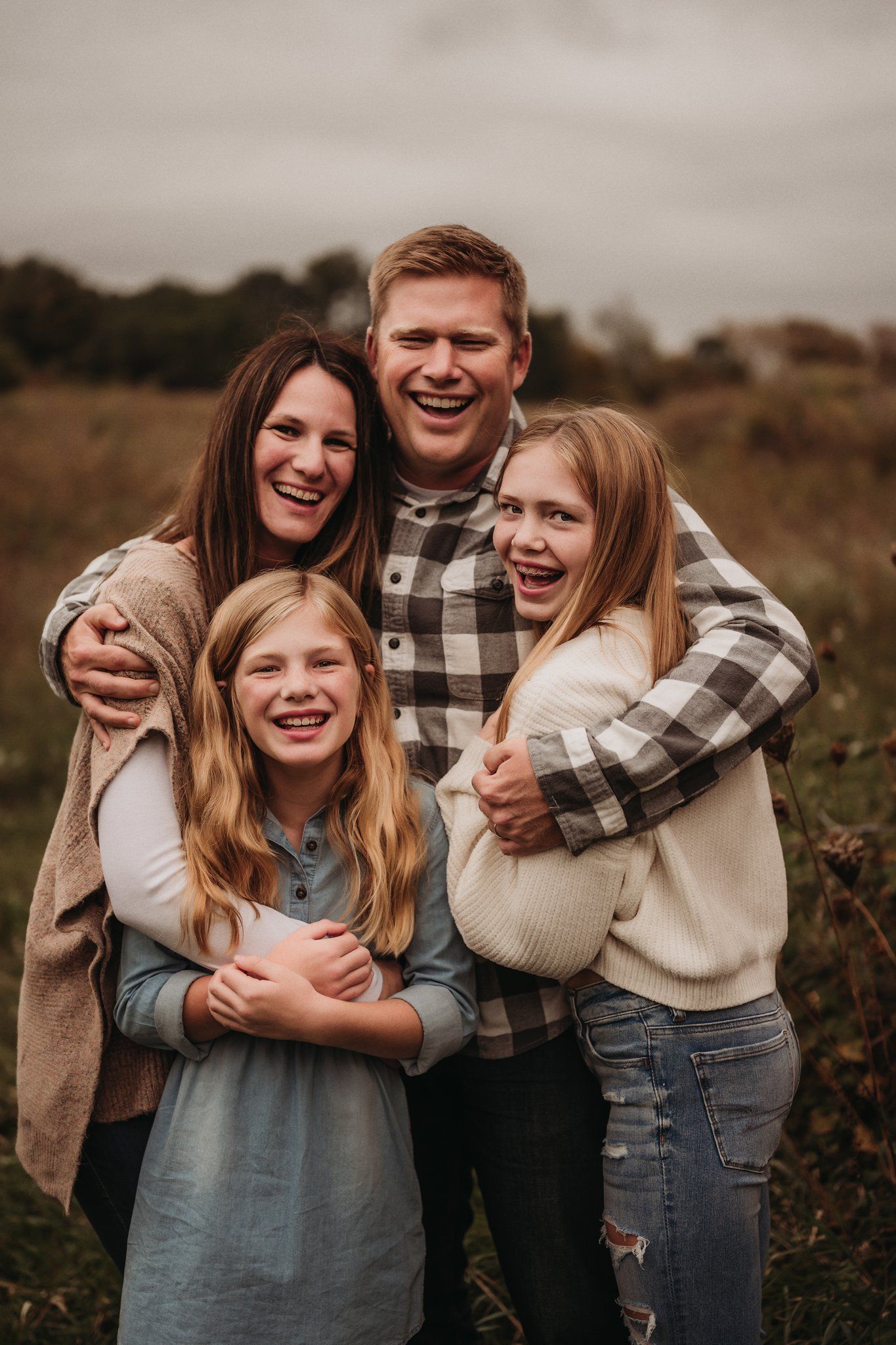 Happy family embraces while sharing genuine laughter in outdoor fall setting.