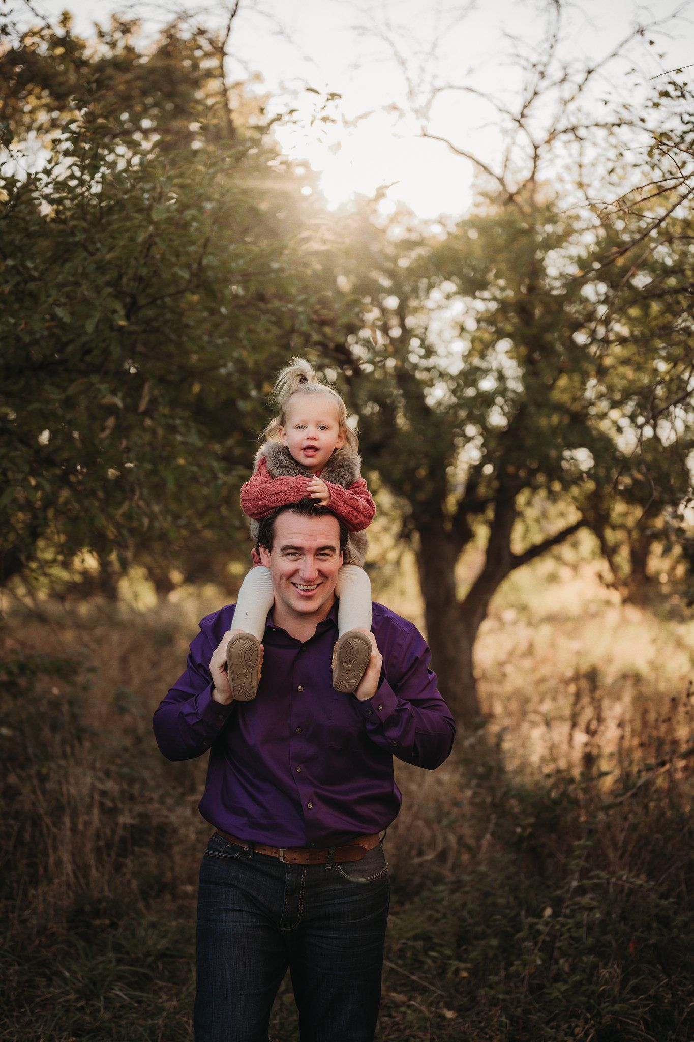 A sunset family photo showing playful shoulder rides in a wooded setting.