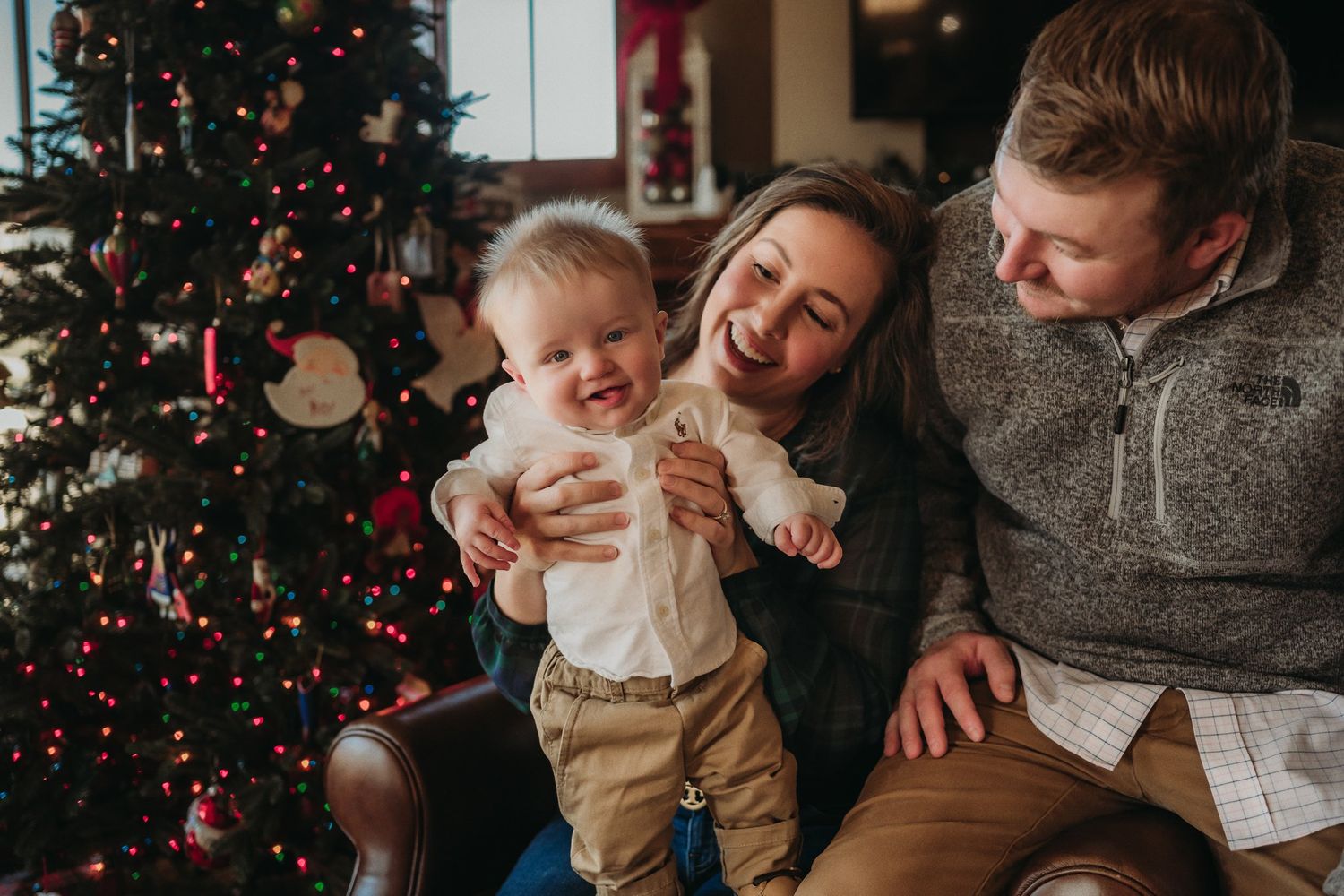 Family laughs together during Christmas photoshoot by decorated tree.