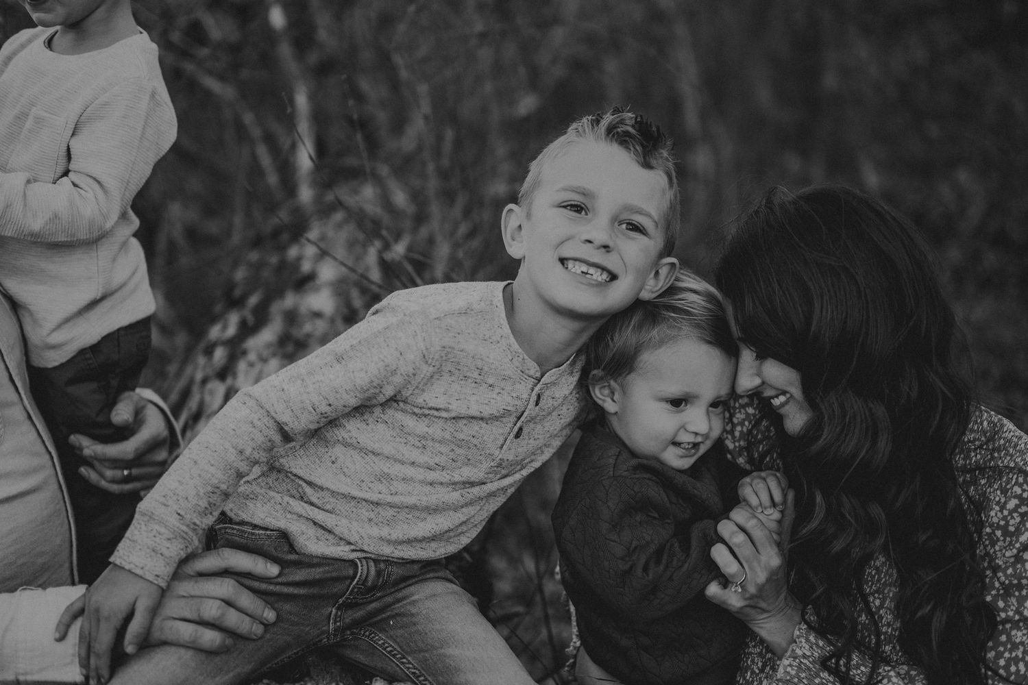 Black and white candid family photo showing tender moments of connection in a forest setting.