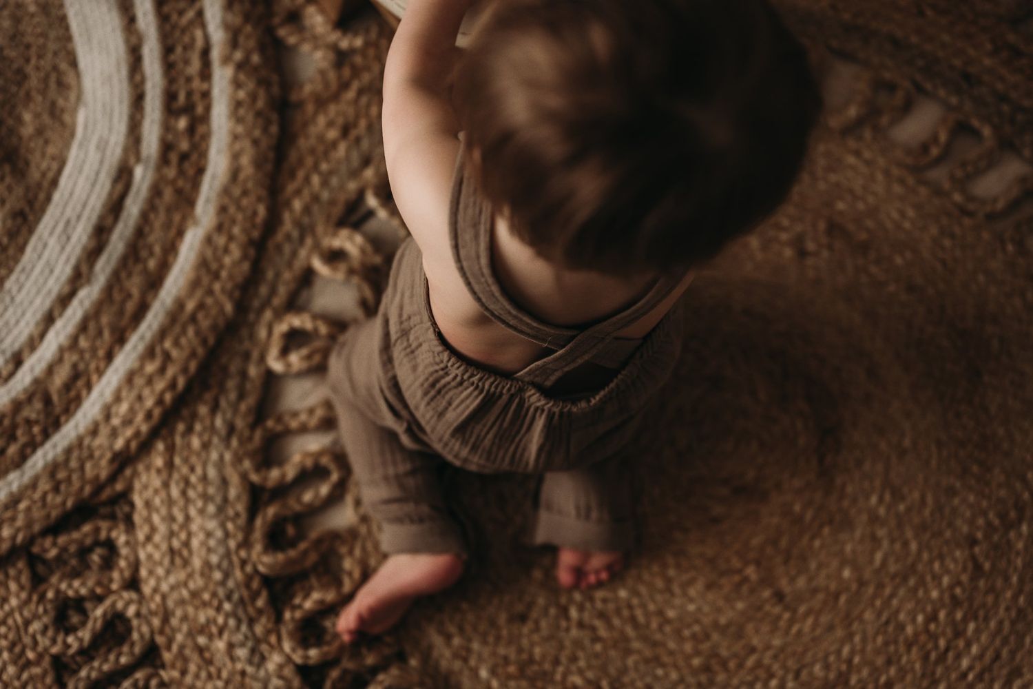 Aerial view of a small child sitting on a circular woven rug in moody lighting.