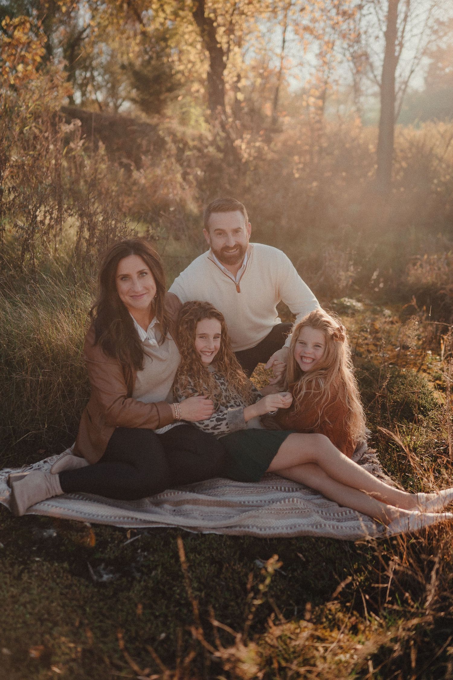 Family relaxing on blanket during sunset outdoor photography session with autumn backdrop.
