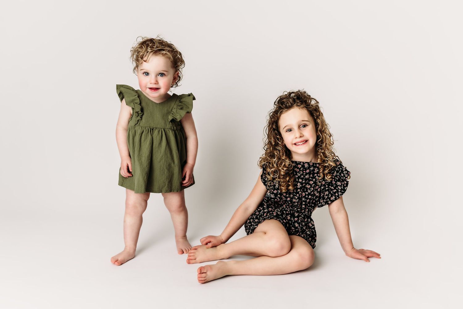 Two children pose together on white backdrop wearing olive green and polka dot outfits.