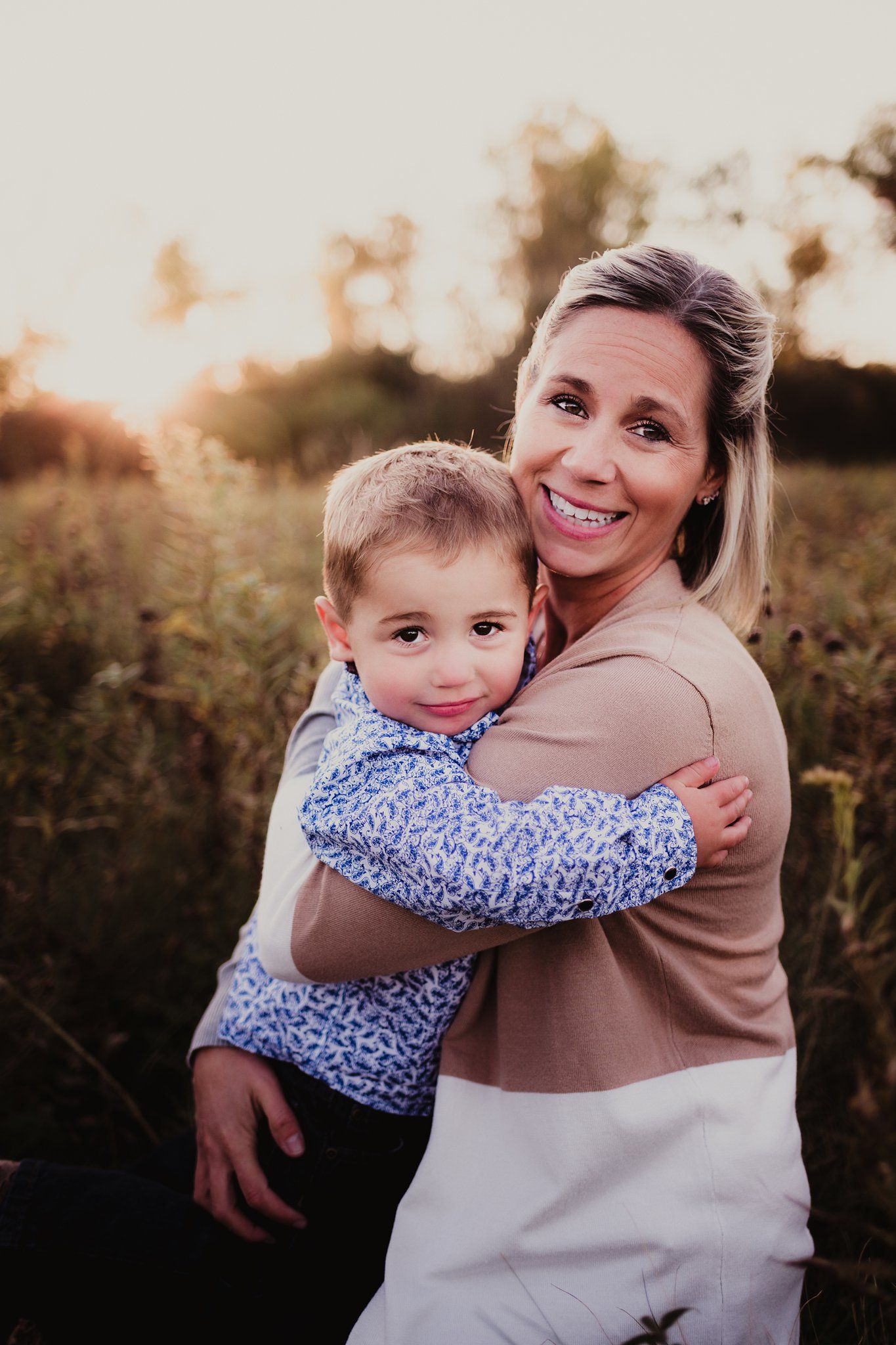 Parent and child embracing in a warm sunset glow against a natural outdoor backdrop.