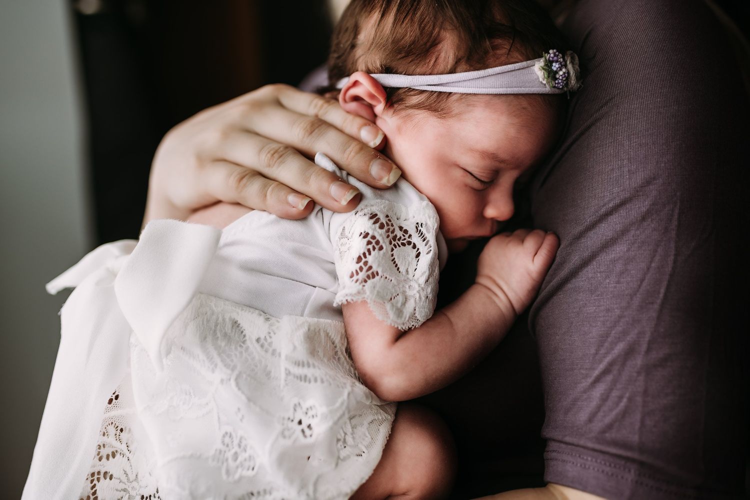 Intimate close-up of a sleeping newborn wearing delicate white lace and a headband.