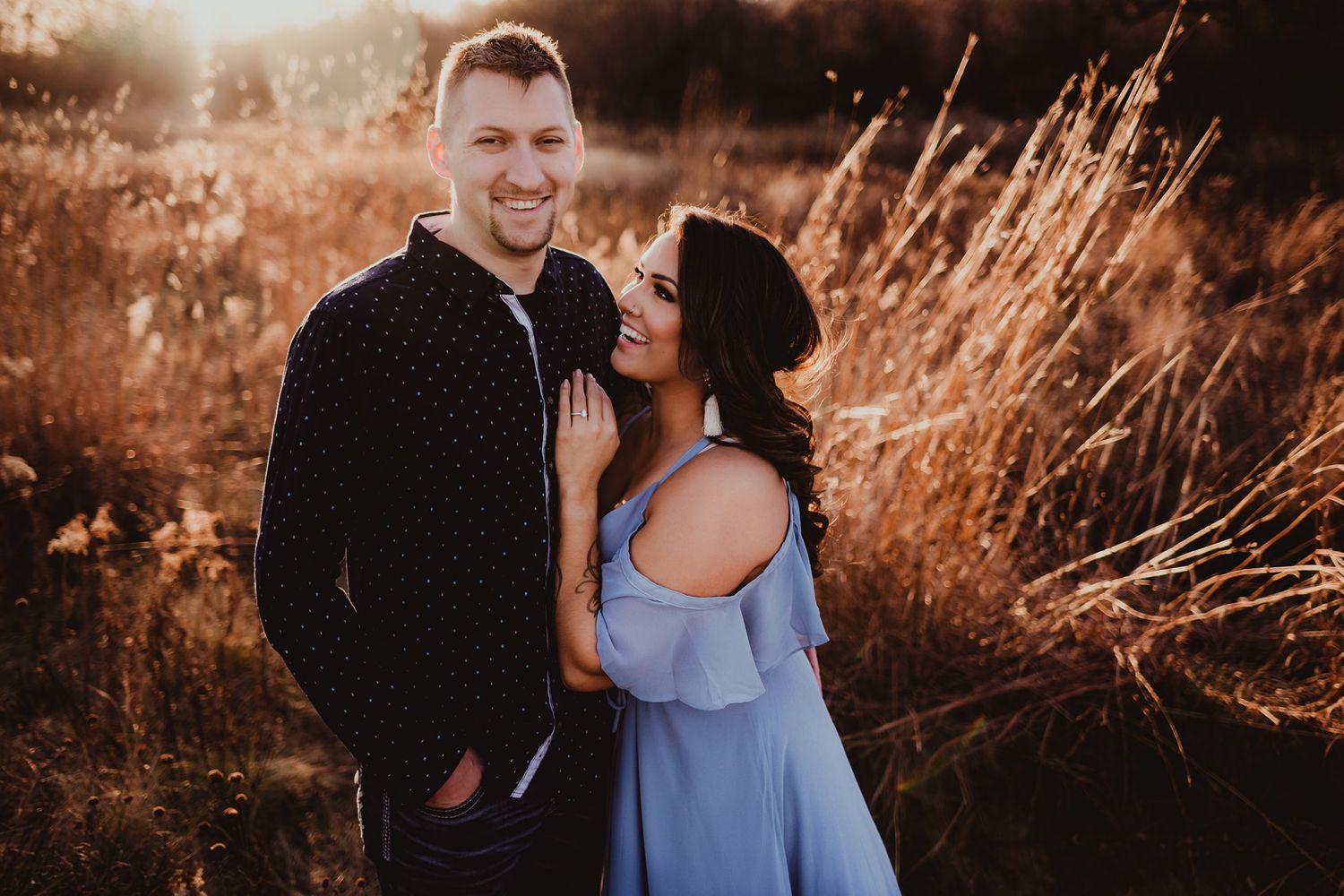 Romantic sunset portrait of couple in blue dress and black shirt against golden grass.