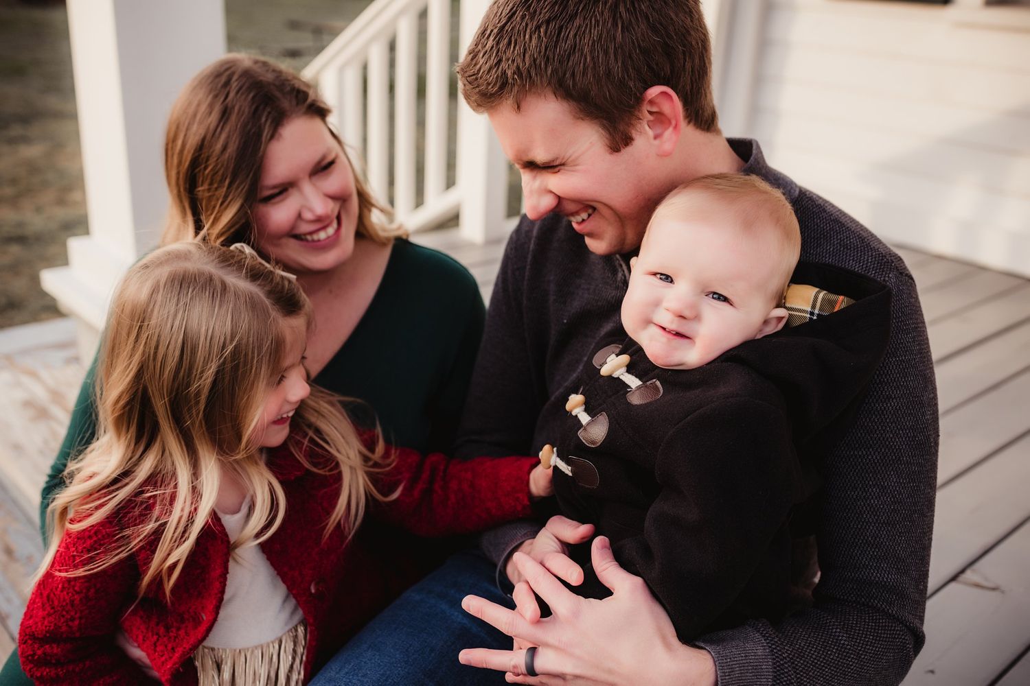 A candid family moment of shared laughter on a white porch during an outdoor photoshoot.
