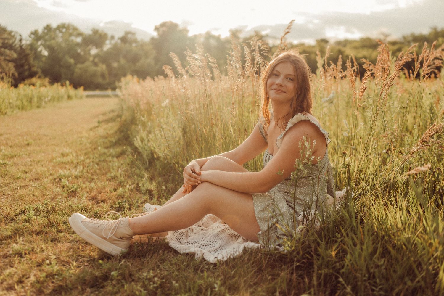 Person in light dress sits casually in wildflower field during sunset wearing white sneakers.