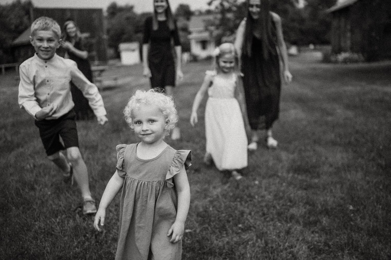 A group plays and runs together on a grassy lawn in a black and white candid shot.