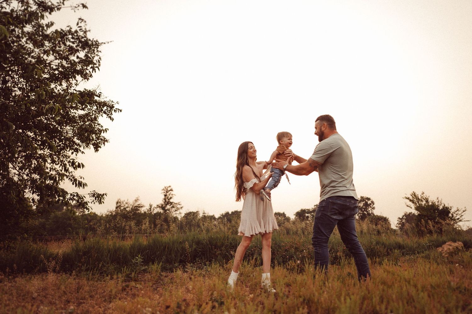 A tender family interaction captured in a sun-drenched field during golden hour.
