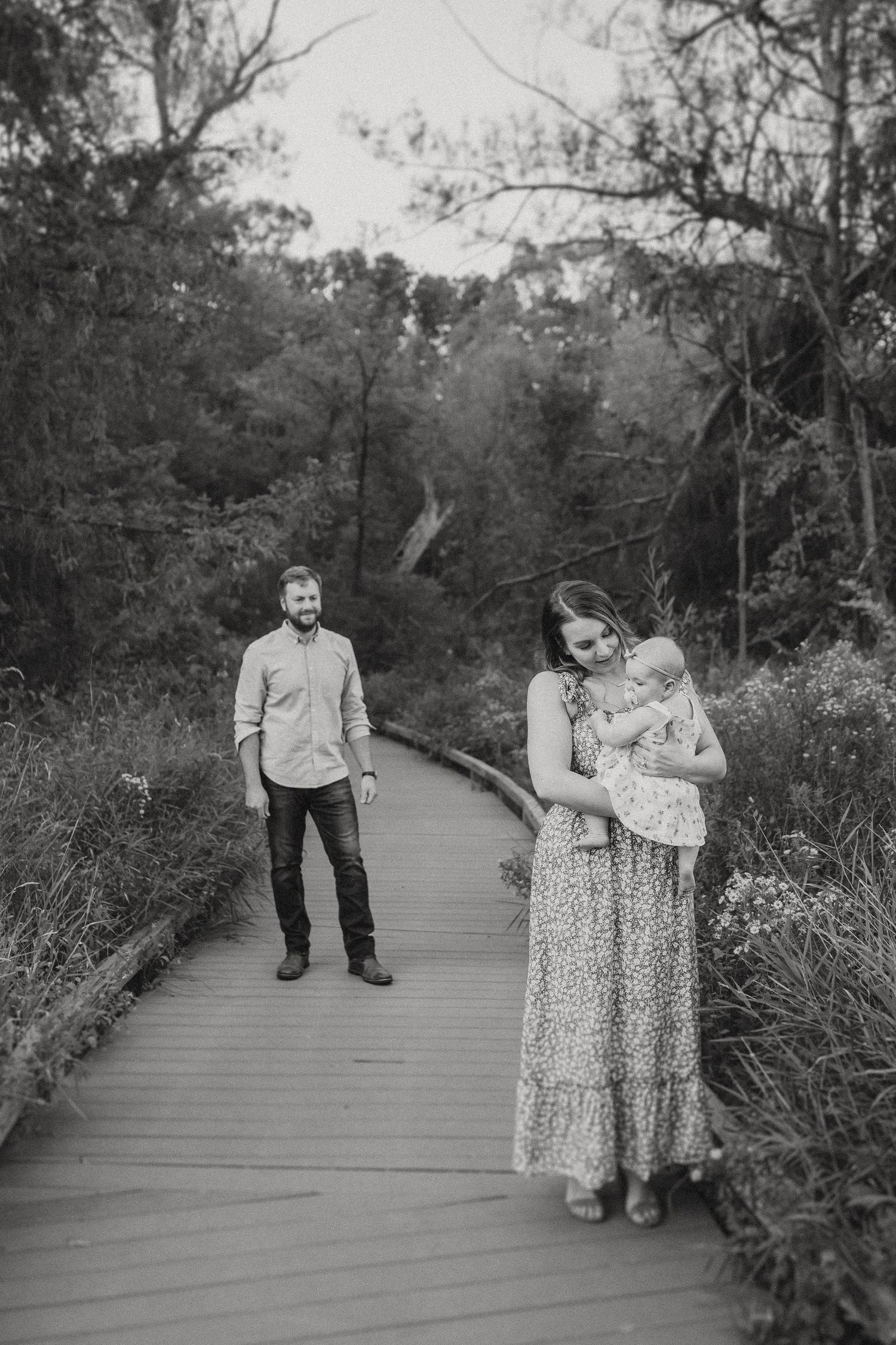 A family walks together on a wooden boardwalk path surrounded by lush forest greenery.