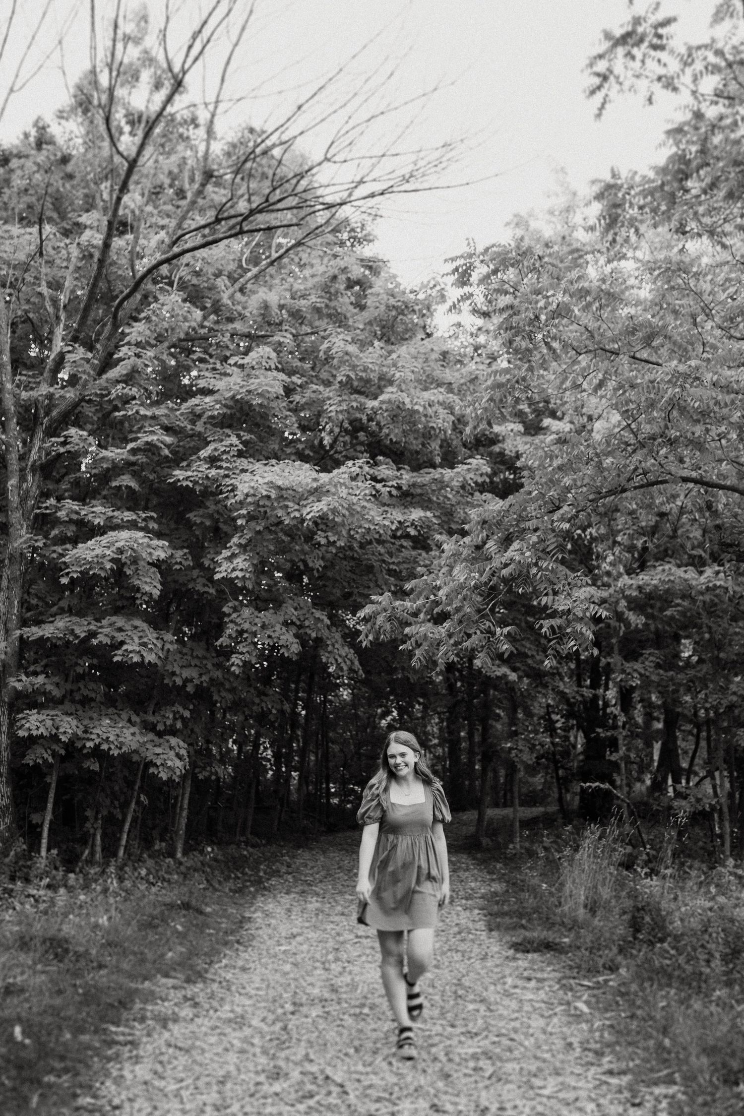 Black and white photograph of someone walking down a tree-lined path in the woods.
