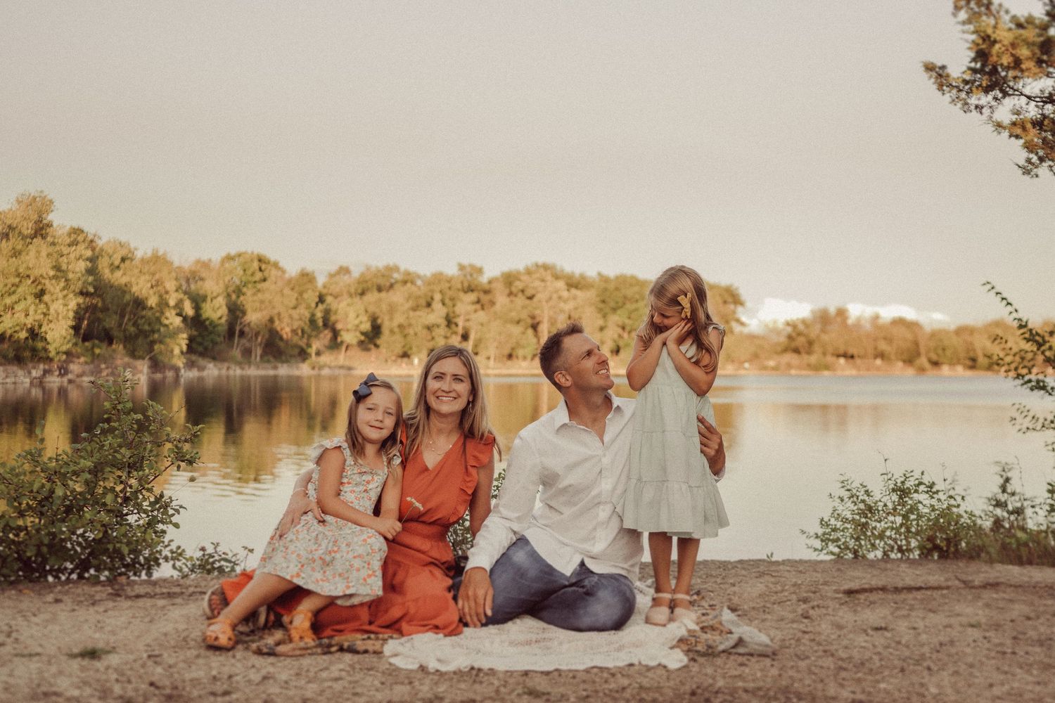 Family gathering at sunset by a serene lake, sitting together on blanket.
