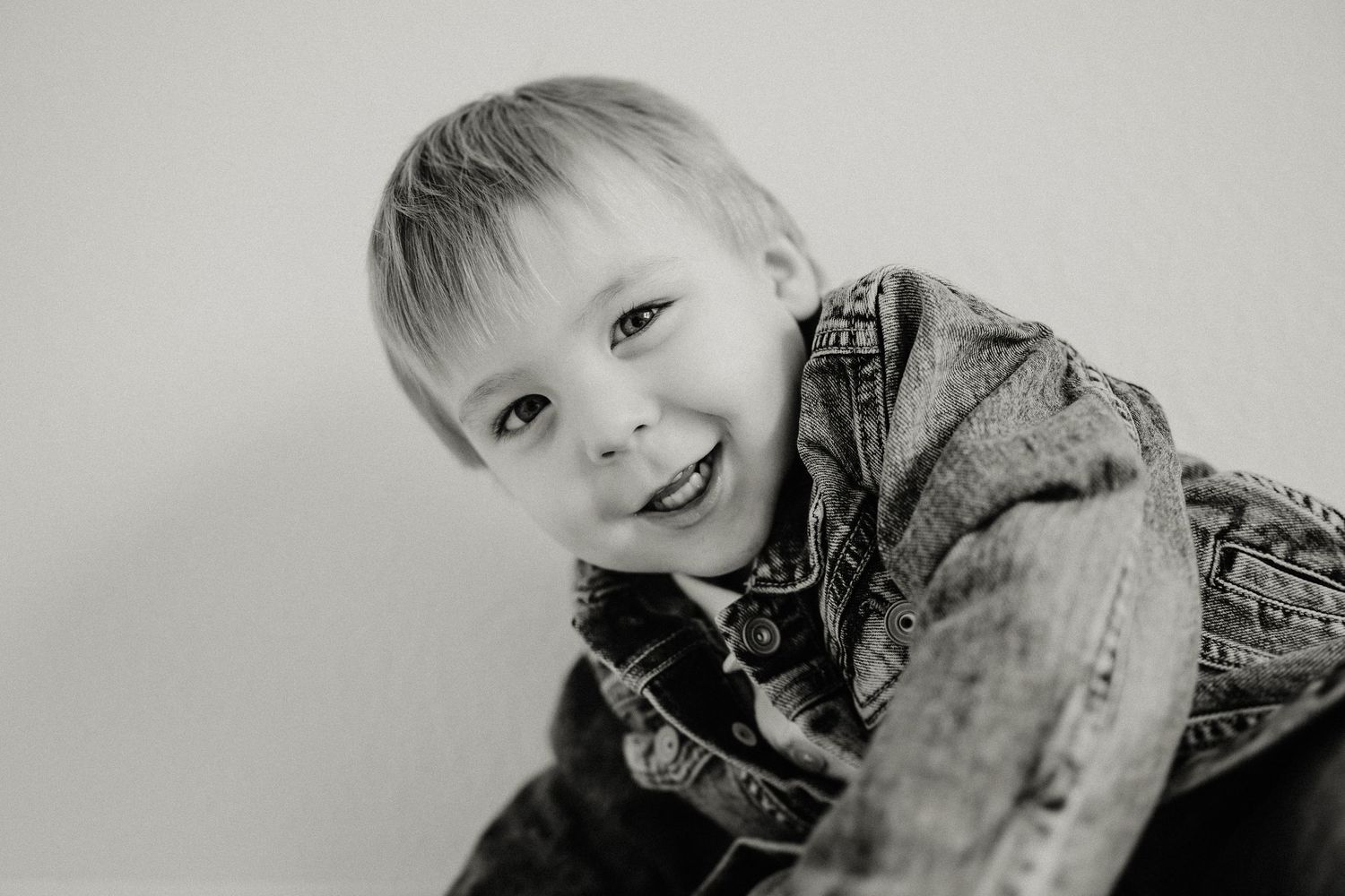 Black and white portrait of child wearing denim jacket with joyful expression.