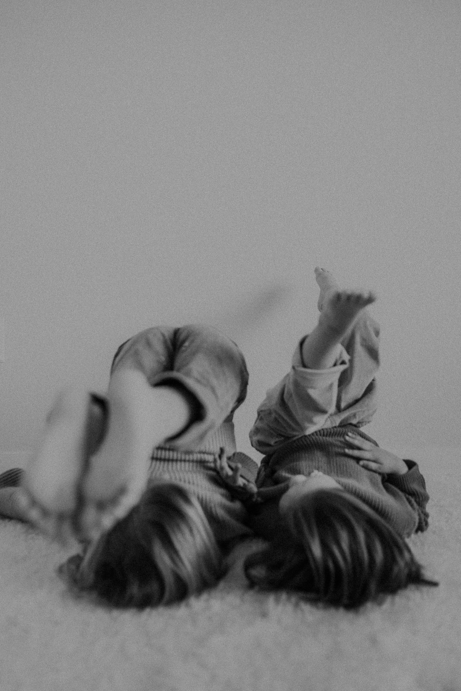 Two figures lying head to head on white carpet in a minimalist black and white photo.