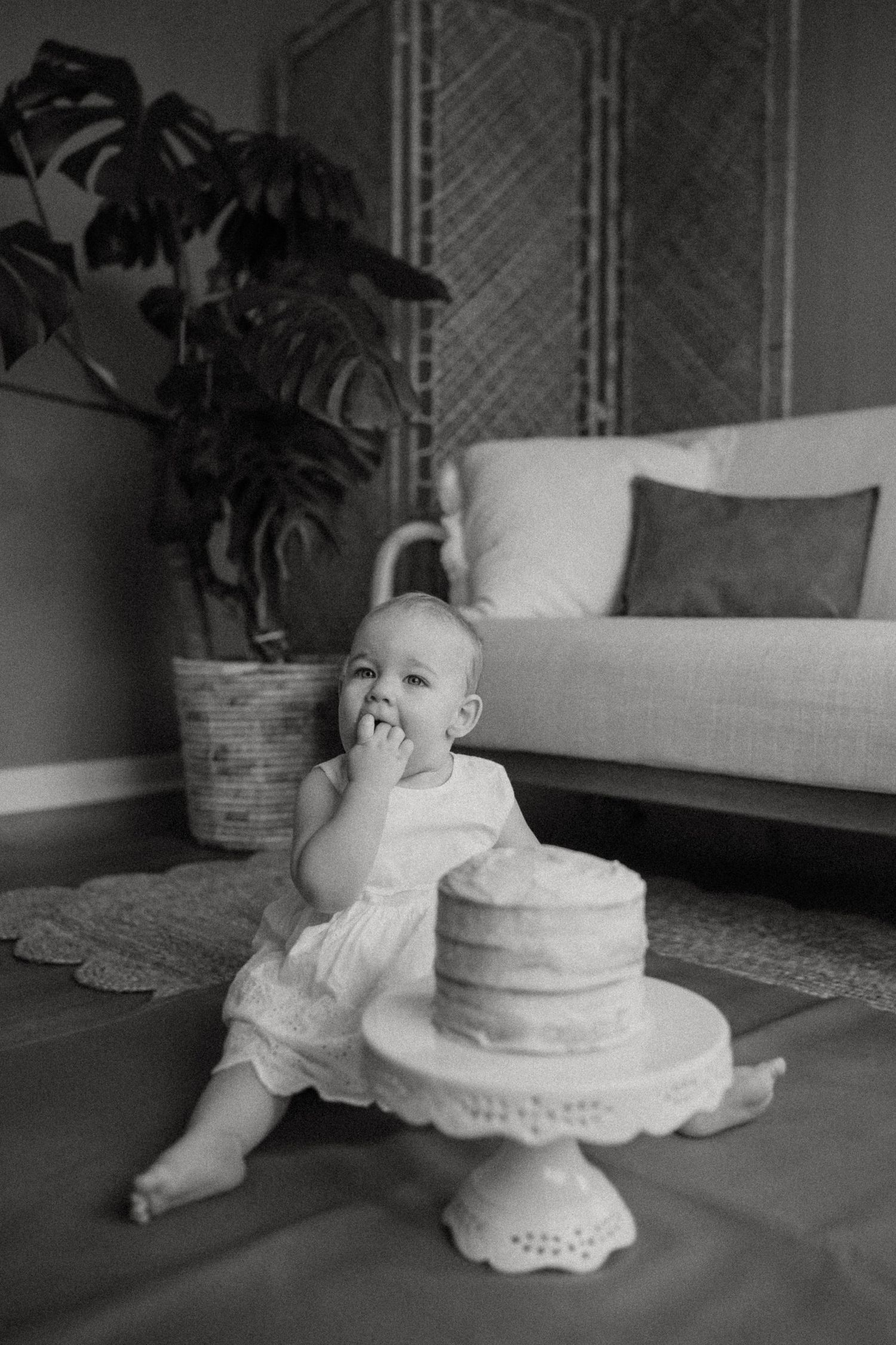 Monochrome portrait of a cake smash photoshoot with a rustic naked cake on a white pedestal.