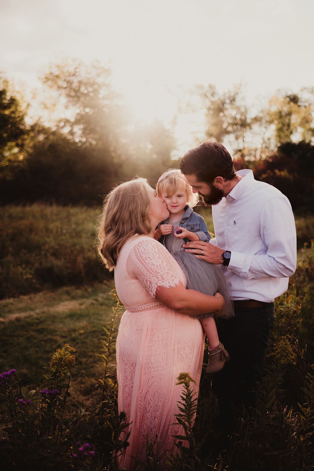 Family photo session at golden hour showing intimate embrace in a wildflower field.