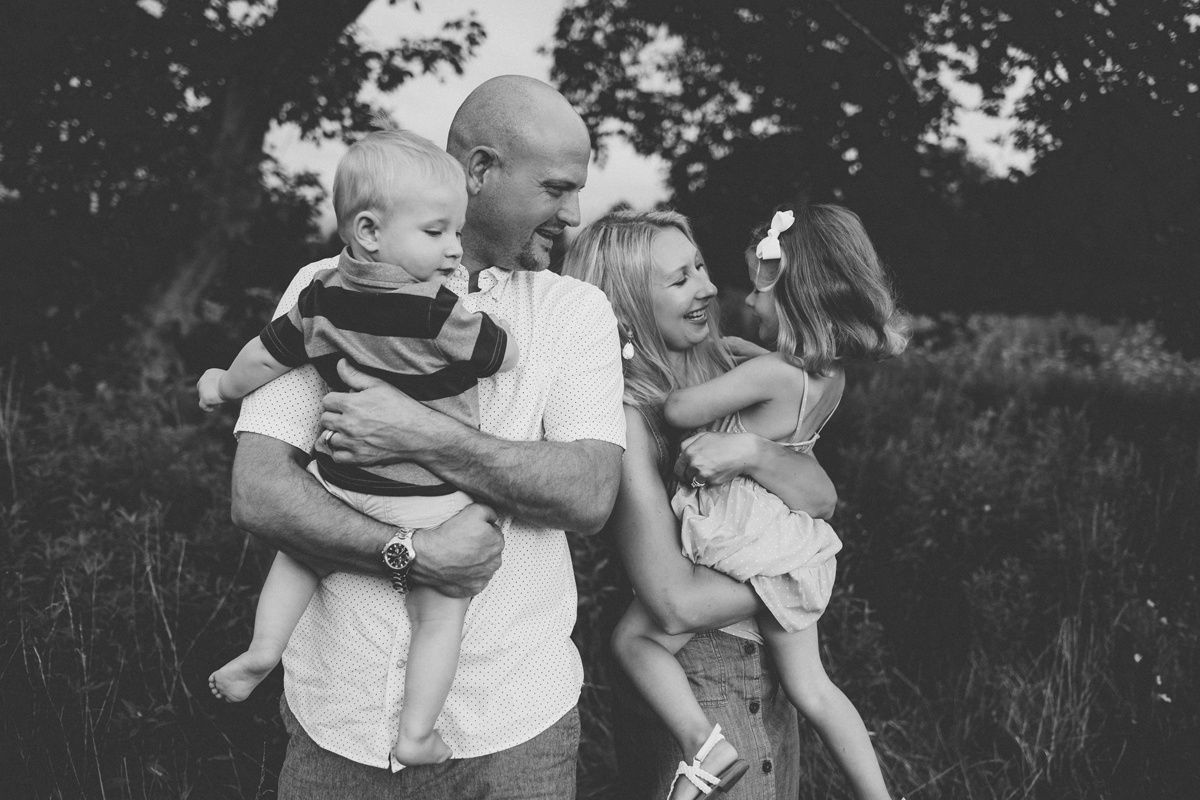 A touching black and white family portrait captured in a natural outdoor setting with tall grass.
