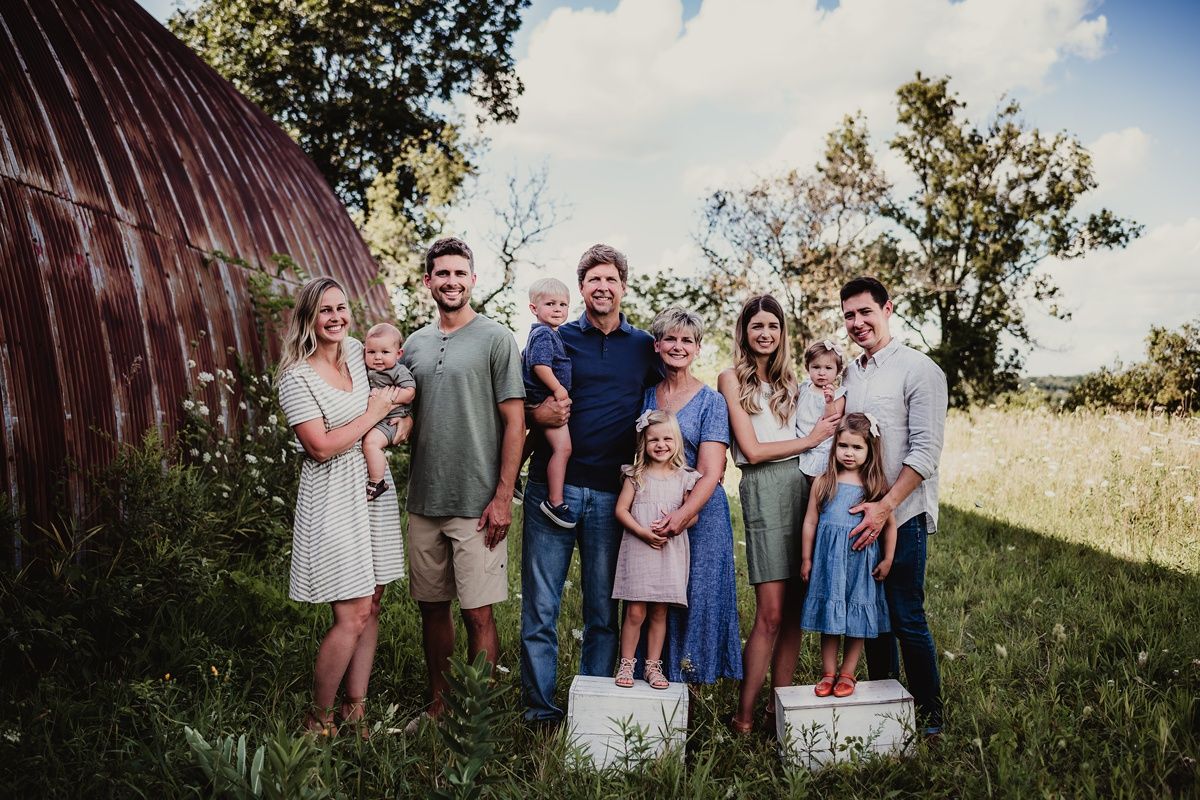 A group portrait of a family standing together outdoors near a rustic barn.