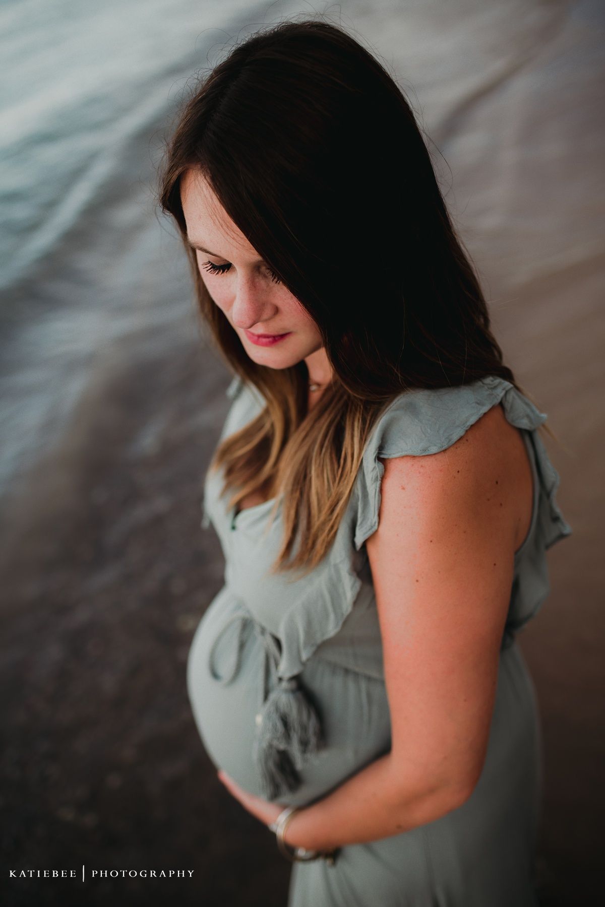 Side profile maternity portrait in soft lighting showing pregnant belly in sage green dress.