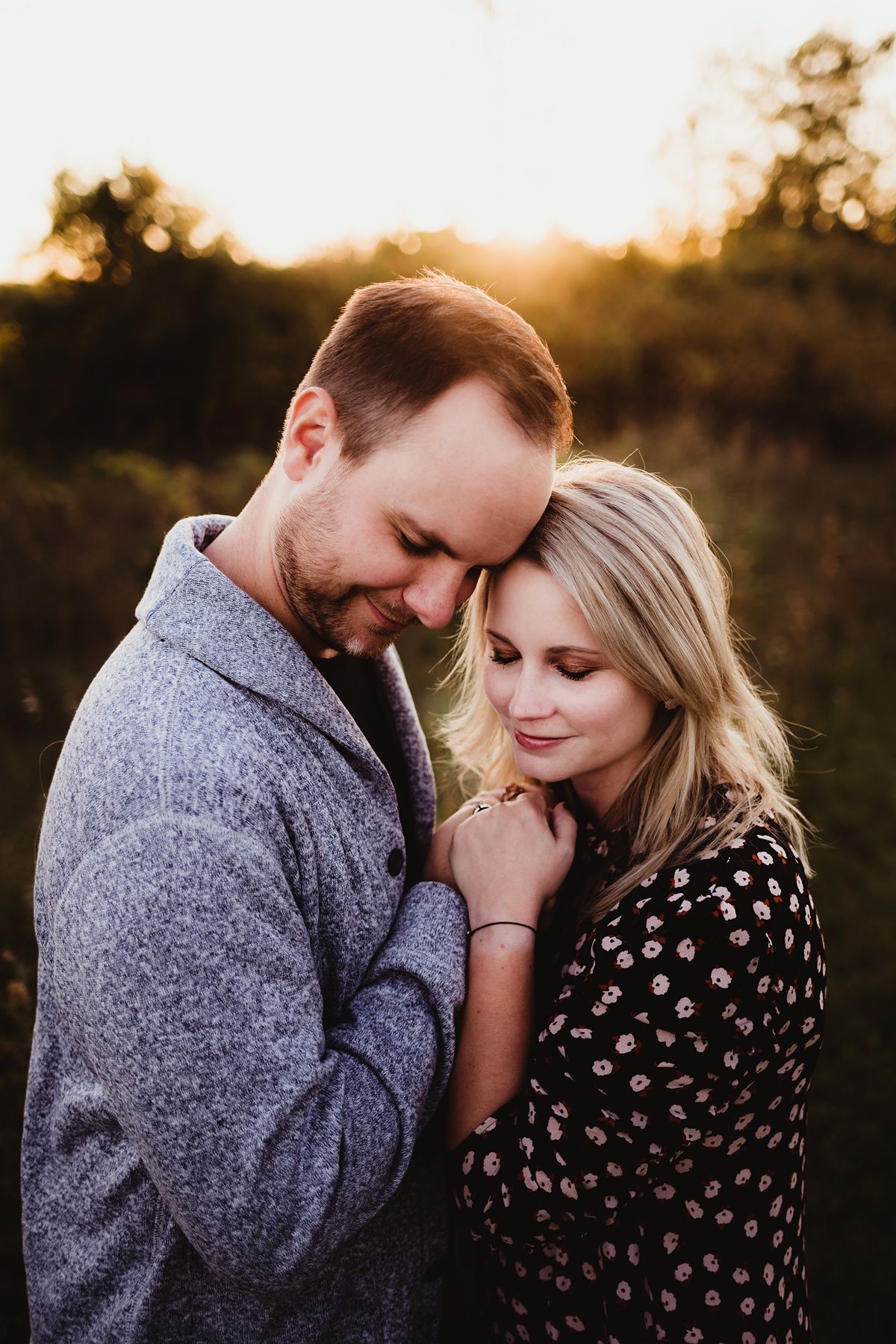 Romantic sunset portrait of couple in close embrace wearing polka dot dress and grey sweater.