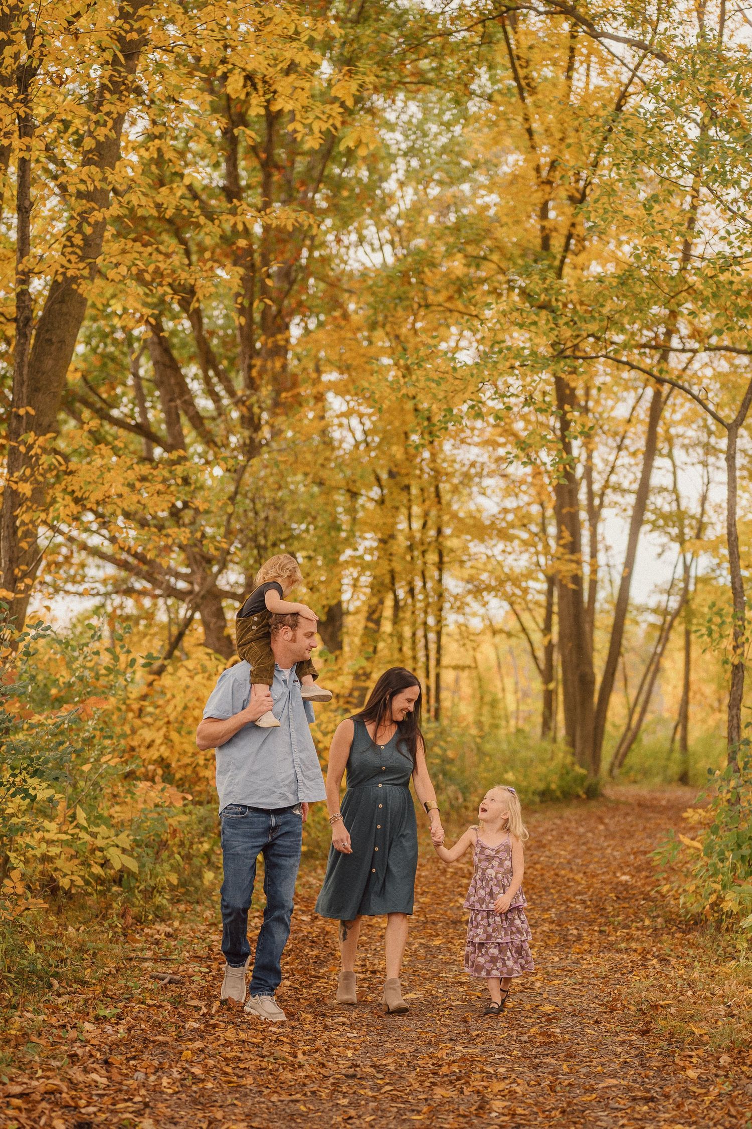 A group walks together along a leaf-covered forest path during peak fall foliage season.