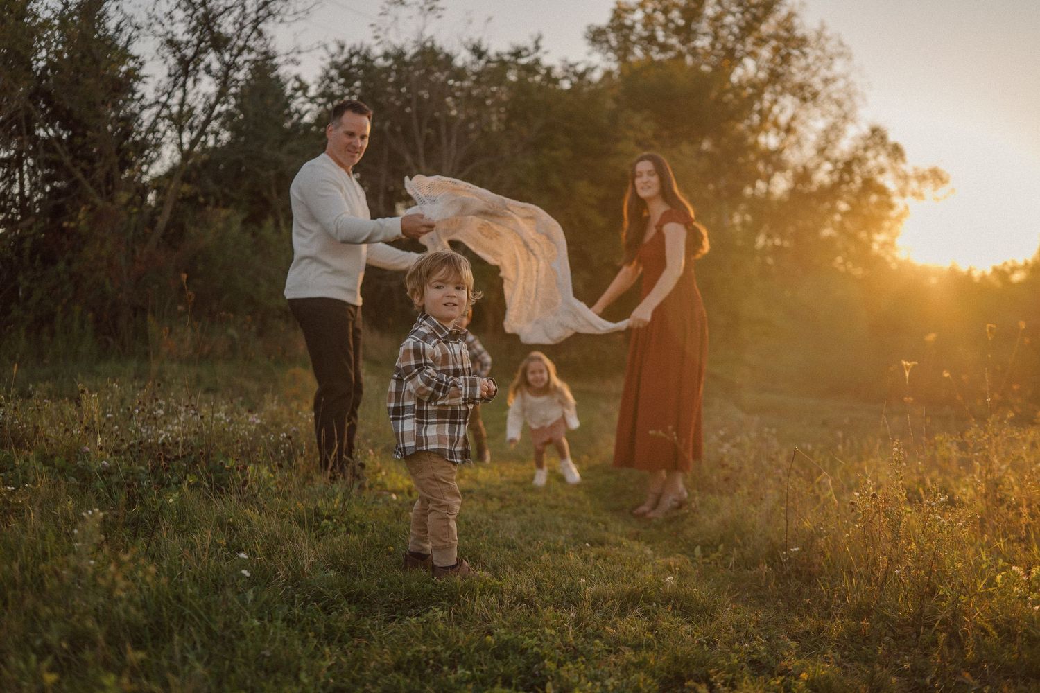Family plays together in a sunlit meadow during golden hour wearing coordinated outfits.