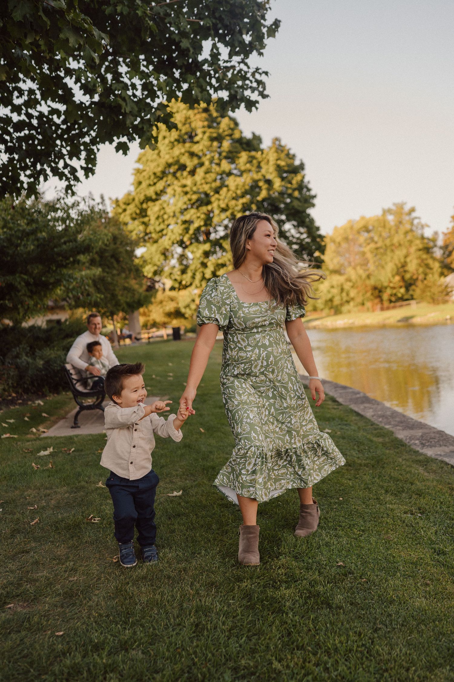 A scenic family moment by a pond at sunset with people in casual attire enjoying time together on green grass.