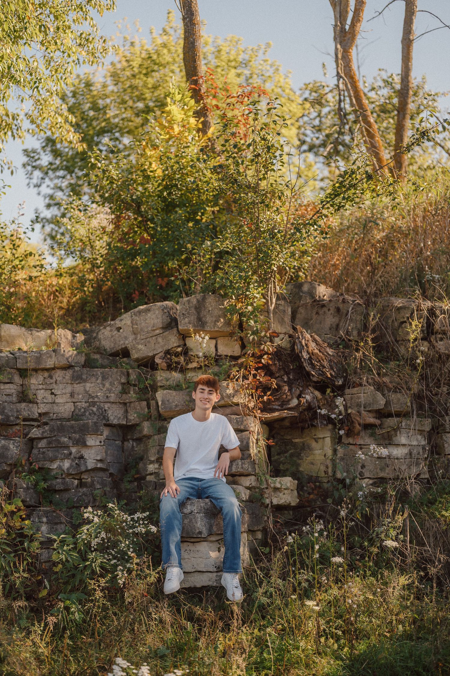 A stone wall provides a rustic backdrop for an autumn outdoor portrait in natural lighting.