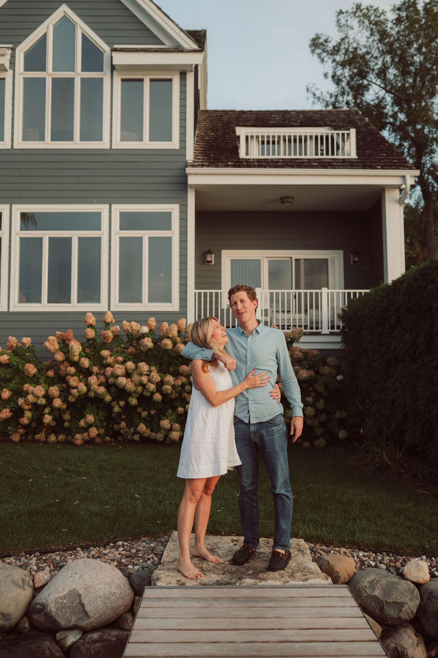 A couple shares romantic moments in front of a house with blooming rose bushes at sunset.